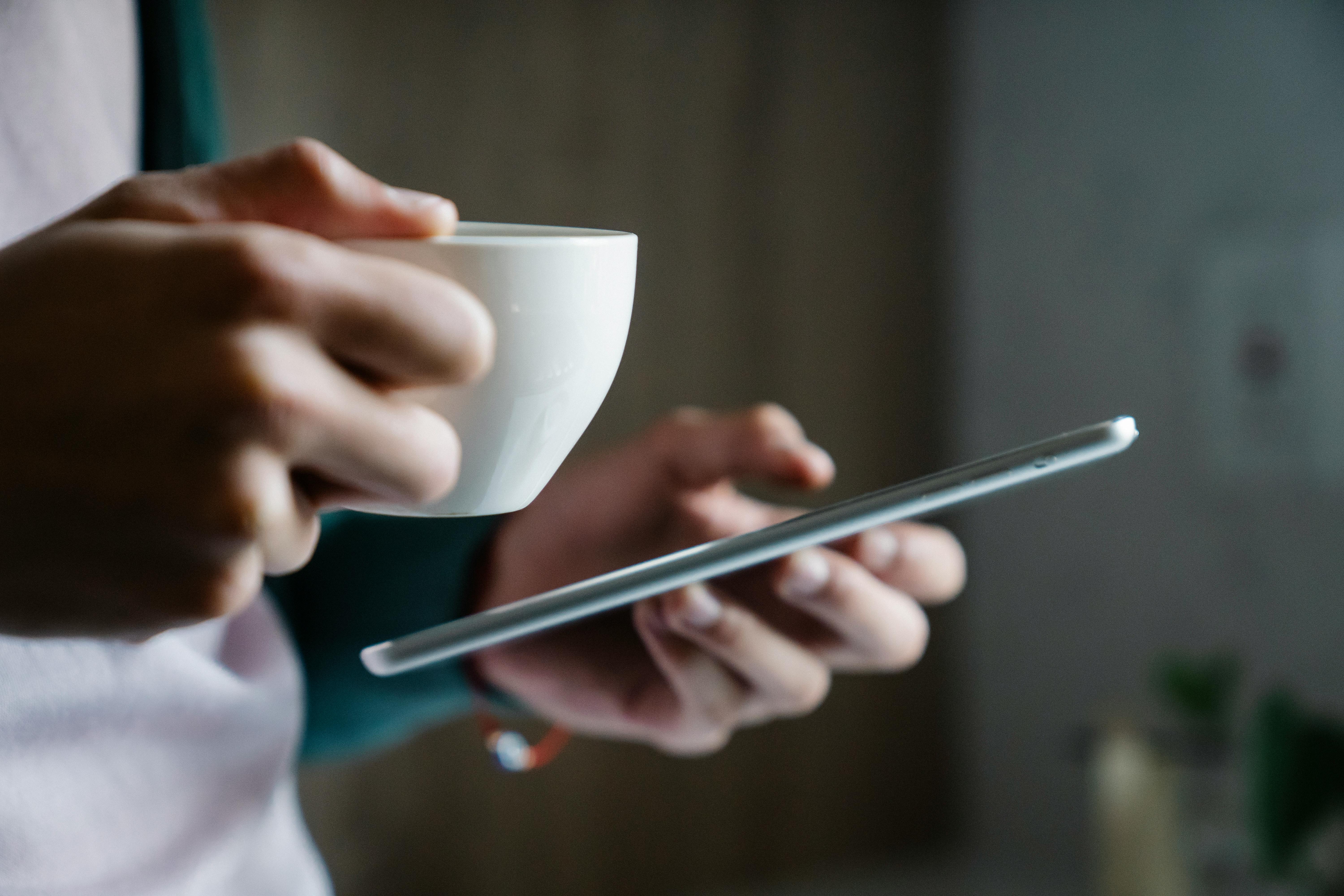 Close-up shot of a person holding a cup of coffee and a smartphone | Source: Pexels