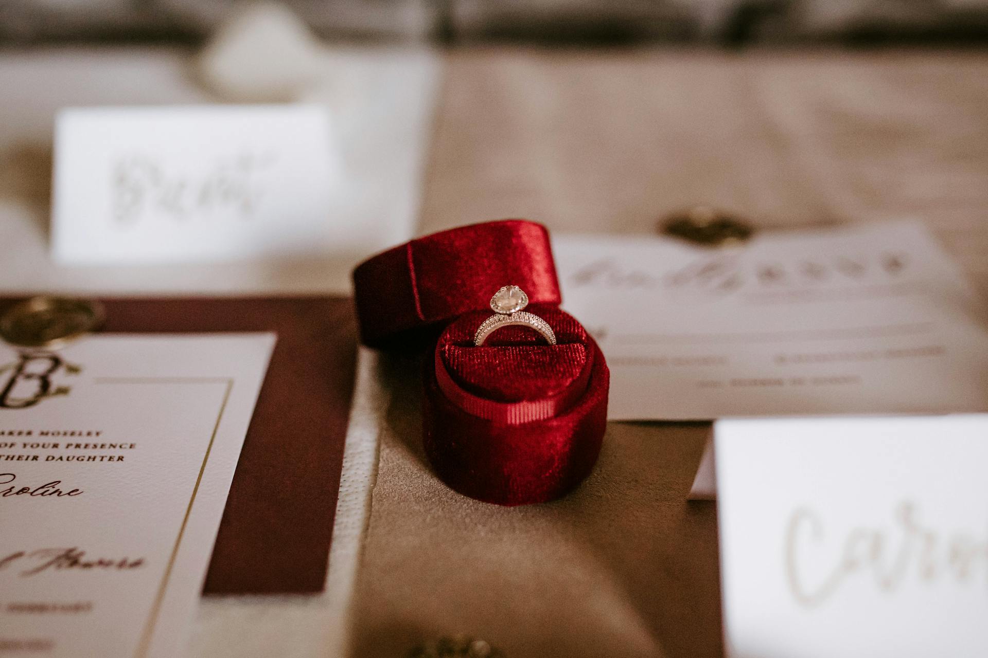 A small red box with a ring placed on a table with wedding invitation cards | Source: Pexels