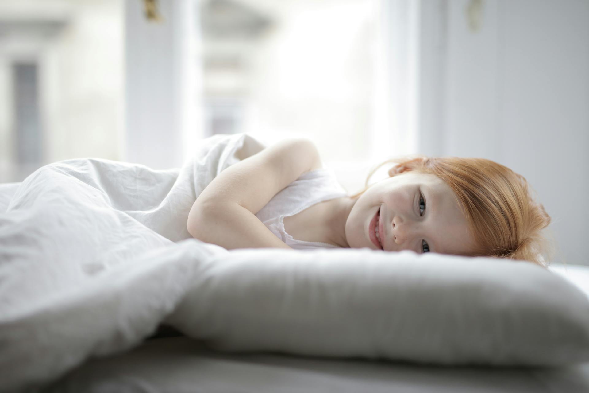 A smiling little girl lying in her bed | Source: Pexels