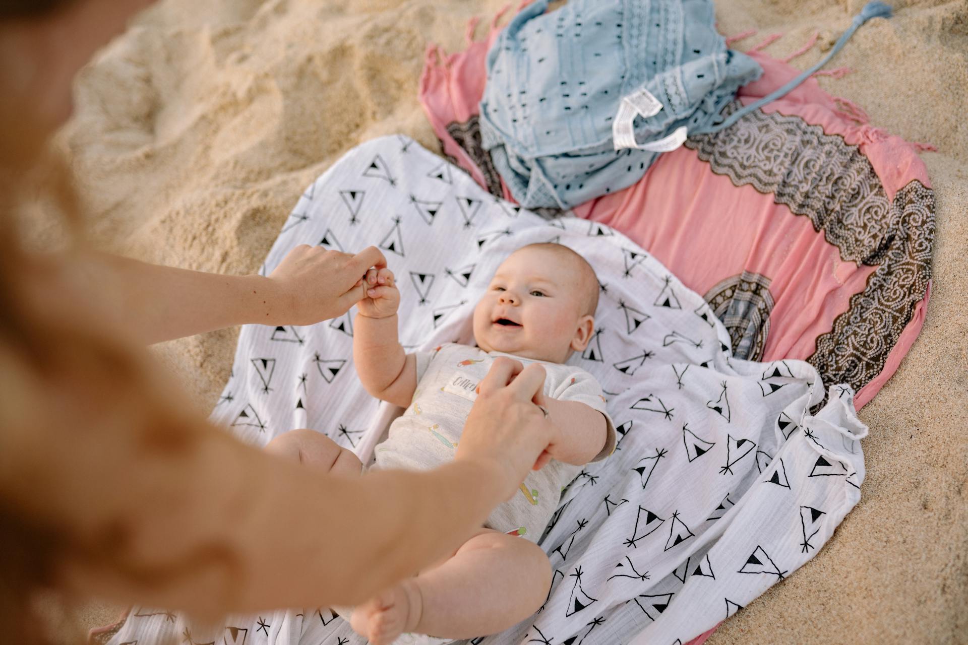 A woman playing with a baby lying on a cloth spread on the sand | Source: Pexels
