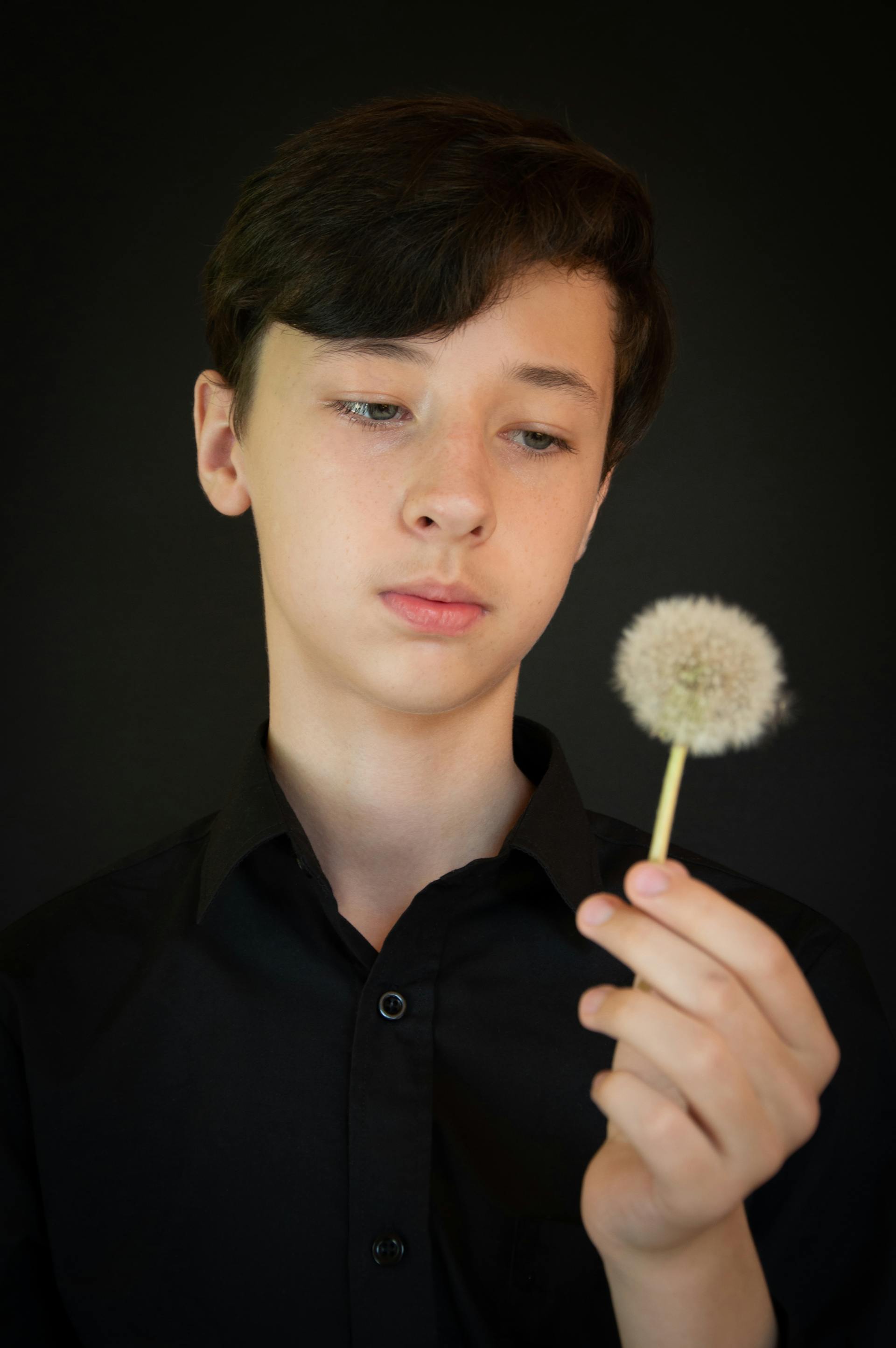 A teenage boy looking at a dandelion in his hand | Source: Pexels