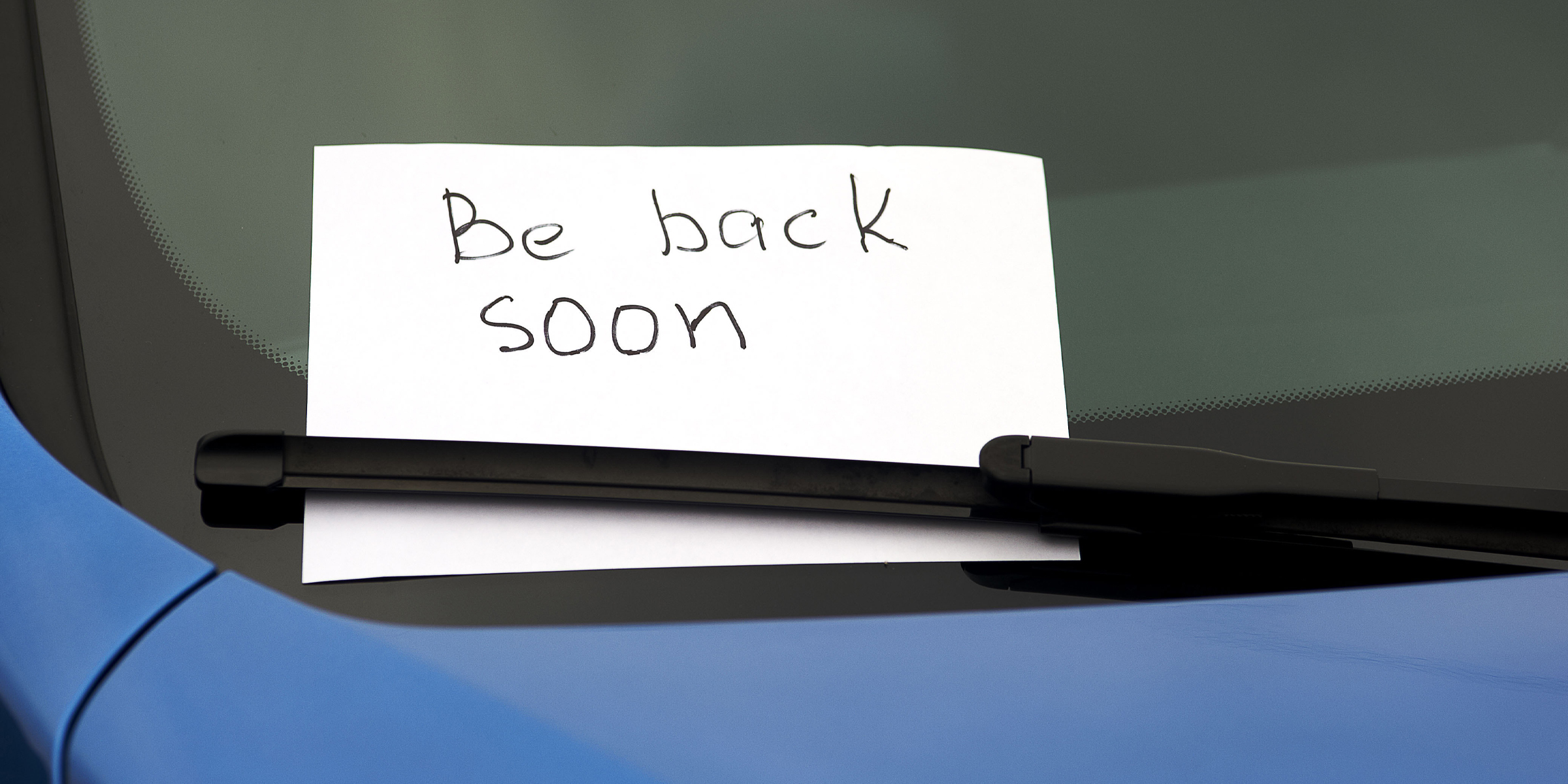 A handwritten note tucked under a car's windshield wiper | Source: Shutterstock