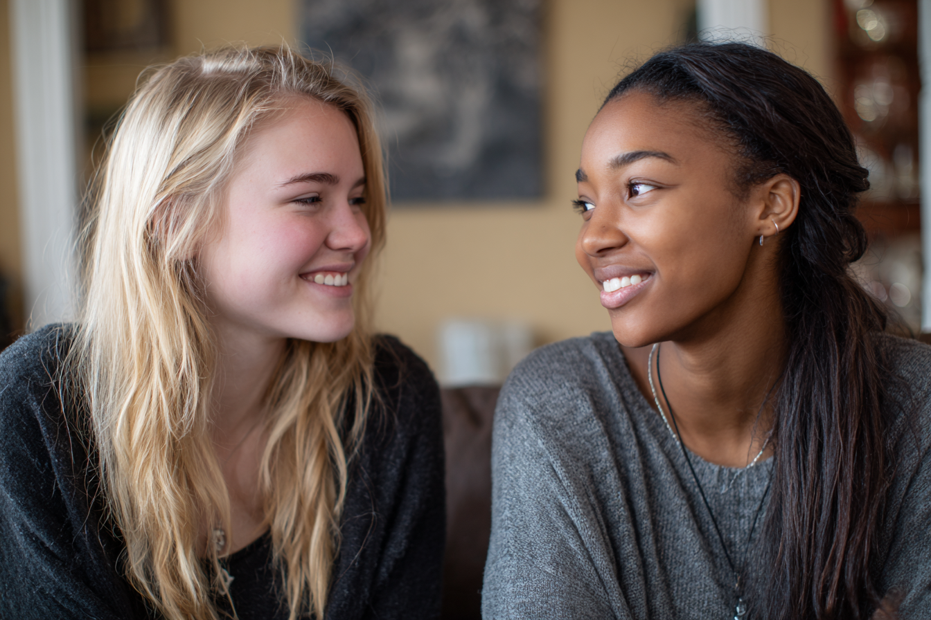 Two teen girls smiling at each other | Source: Midjourney