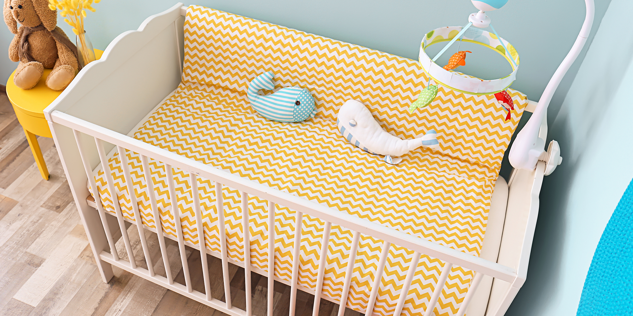 A baby crib with yellow chevron bedding and plush toys tucked in a bright nursery corner | Source: Shutterstock
