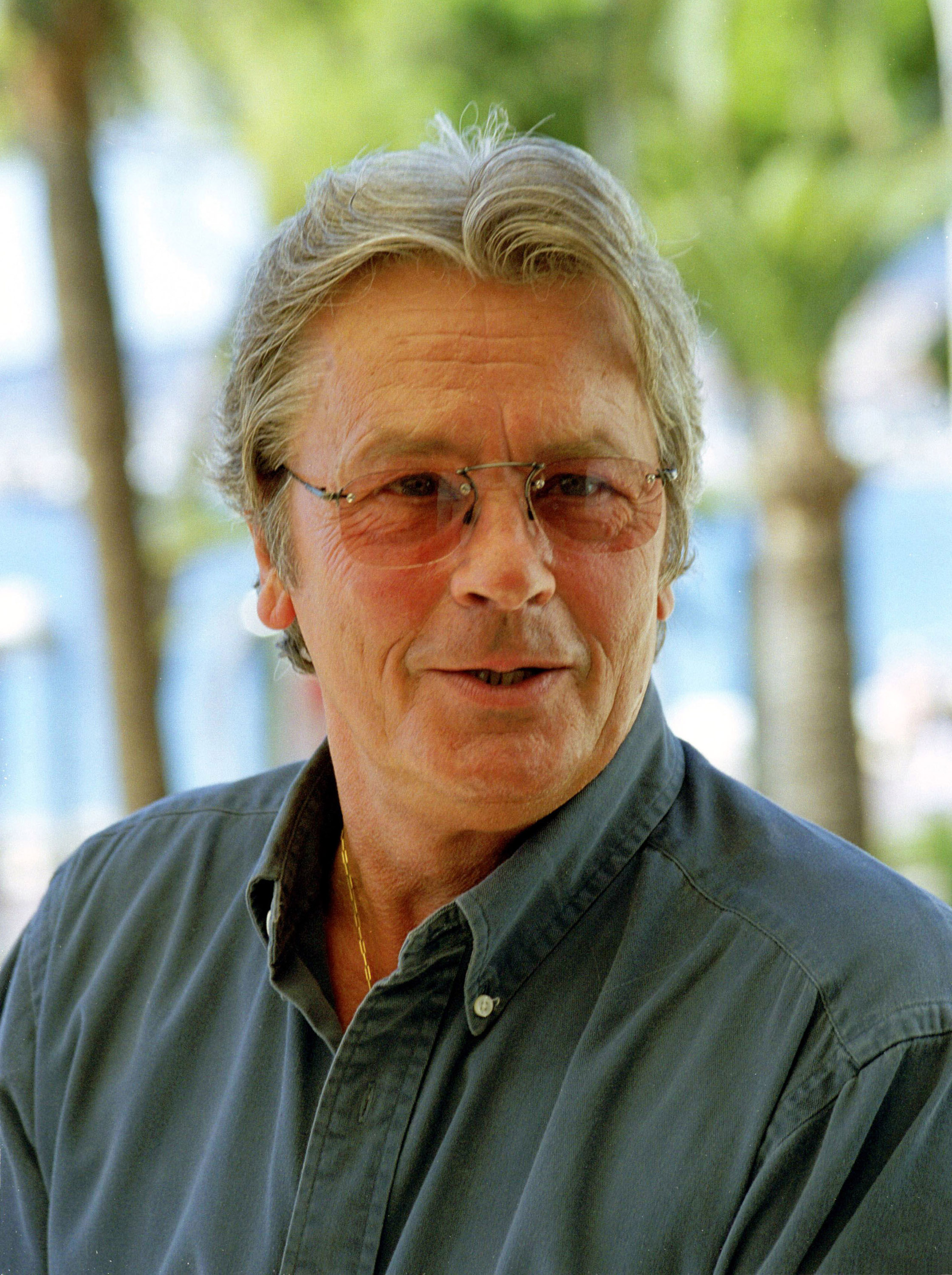 Delon, who turned 65 in 2000, still carried the mystique that made him an icon of European cinema. In a relaxed moment, he wore tinted glasses and an open-collar shirt, his tousled silver hair and quiet confidence lending him the look of a man who had nothing to prove. The image captured an aging legend, unfussy and effortlessly charismatic.