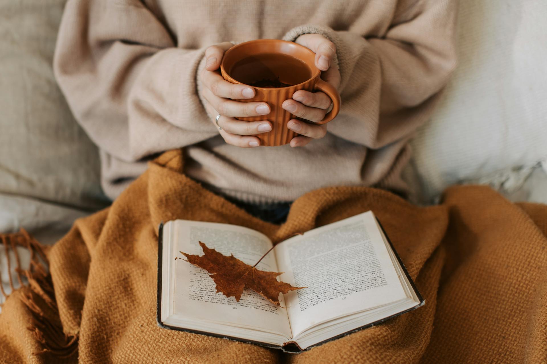 A closeup shot of a woman holding a cup of tea and reading a book | Source: Pexels