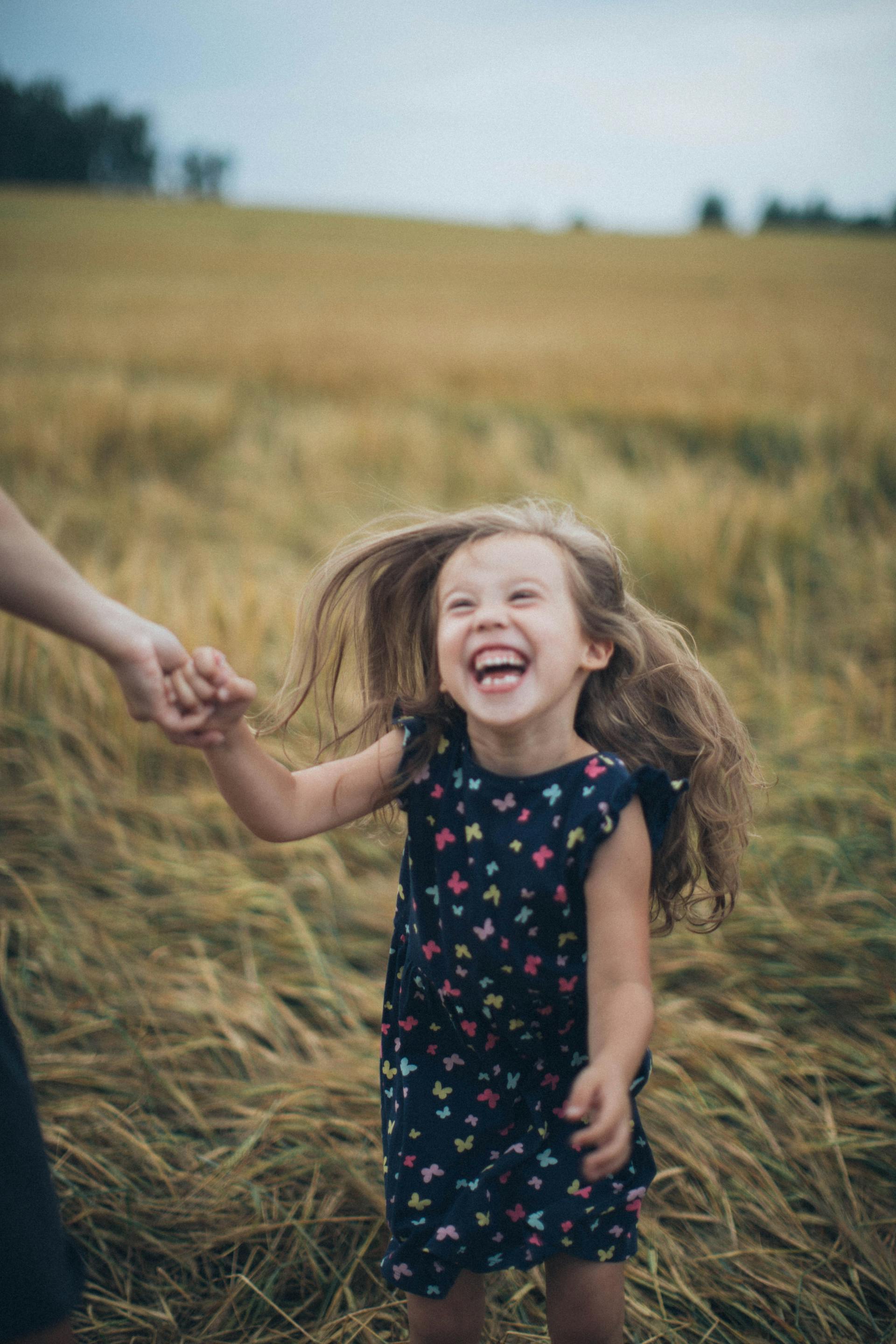 A smiling little girl holding her mother's hand in a field | Source: Pexels