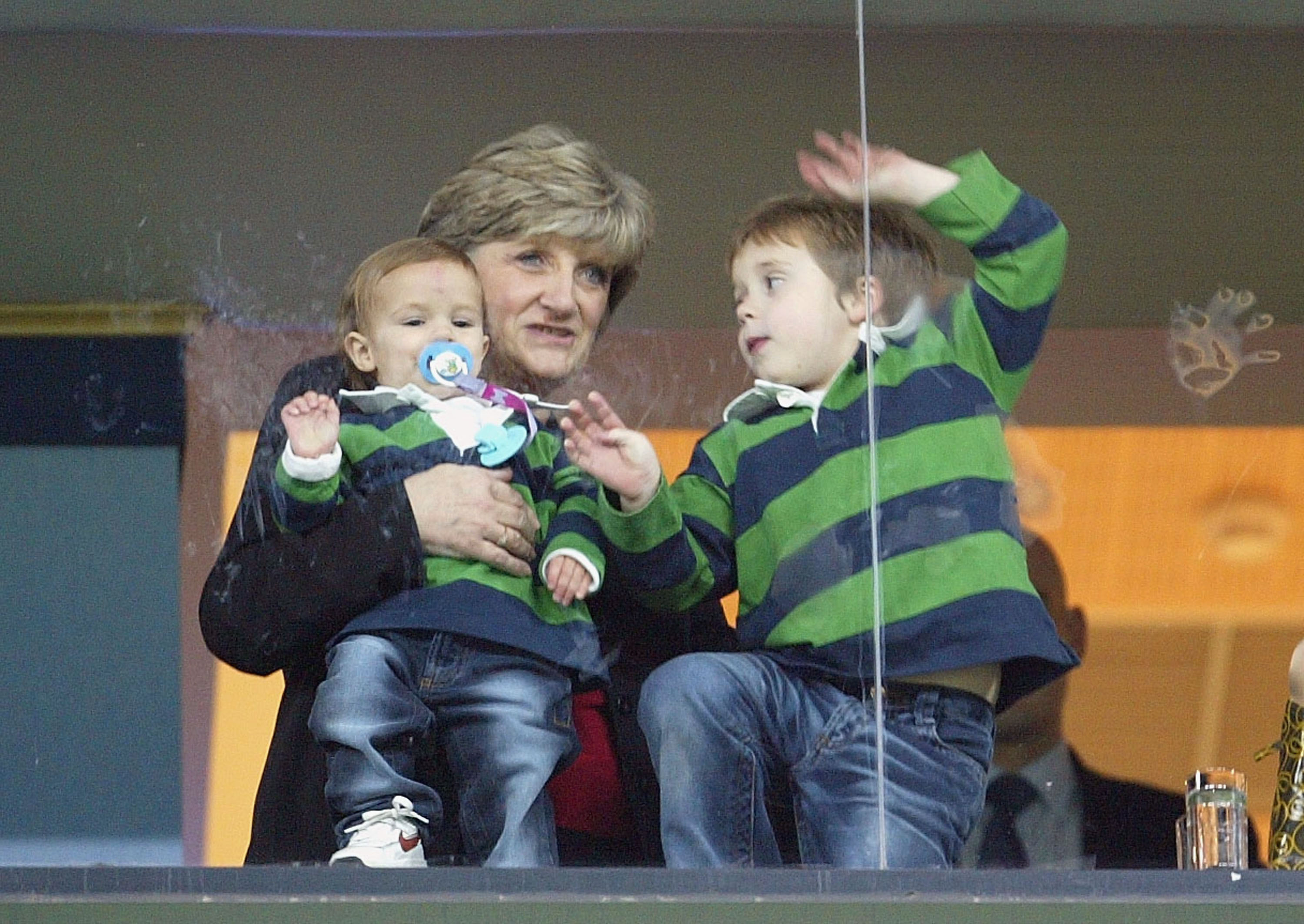 Brooklyn and Romeo watch their father David Beckham of Real Madrid with their grandmother during the Spannish Premier Leage match between Real Madrid and Atletico Madrid at the Bernabeu Stadium on December 3, 2003 in Madrid, Spain. | Source: Getty Images