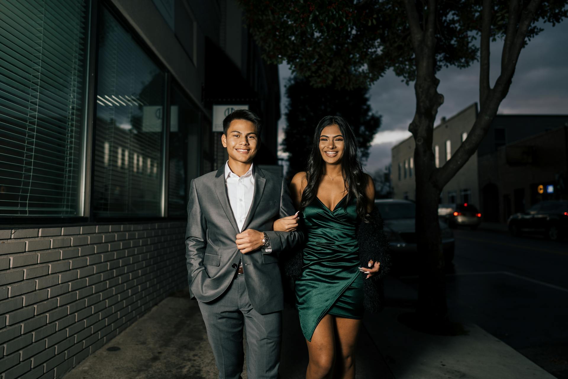 A happy young couple dressed up and walking arm in arm on a city street at night | Source: Pexels
