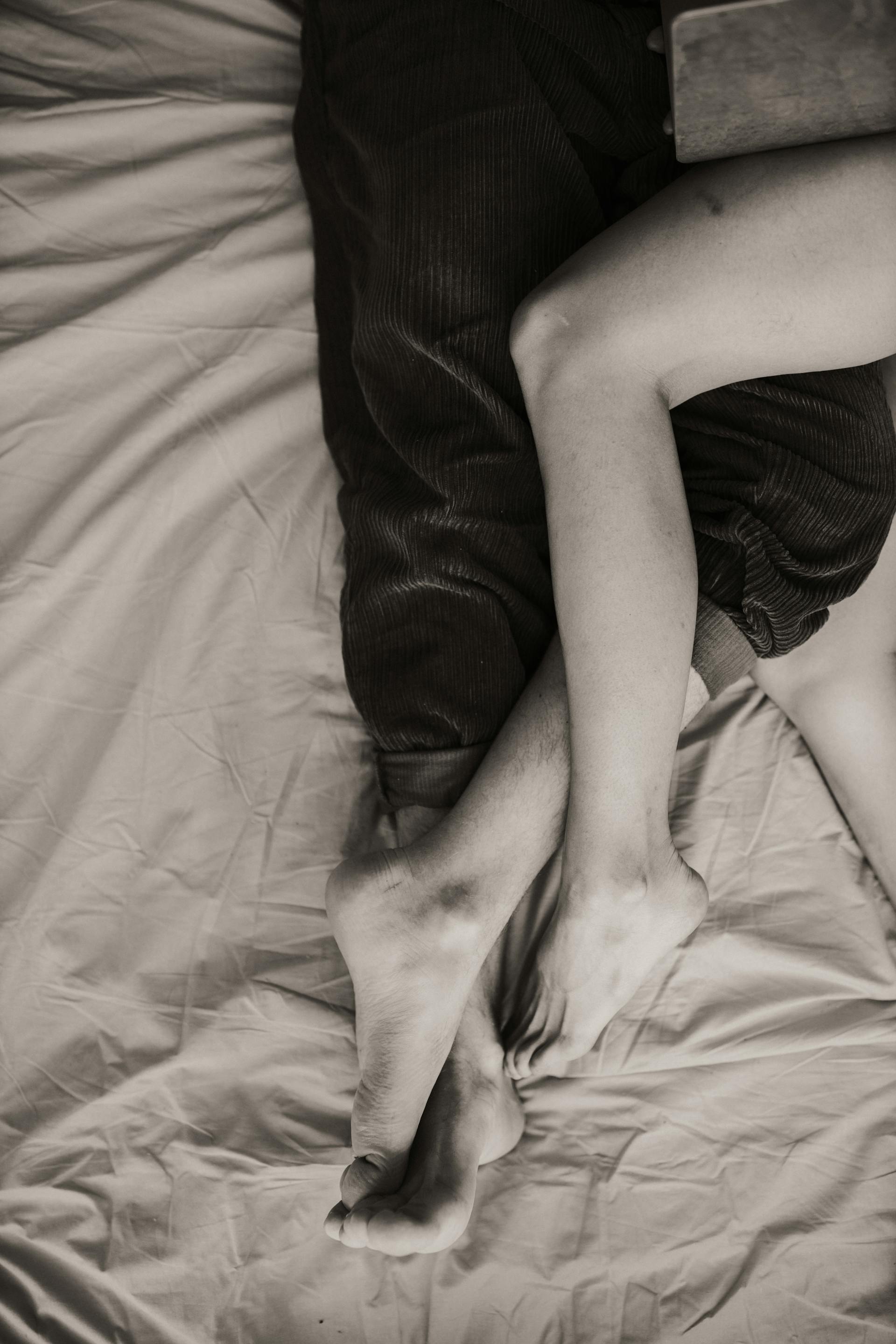 Two people lying on a bed with their legs intertwined | Source: Pexels