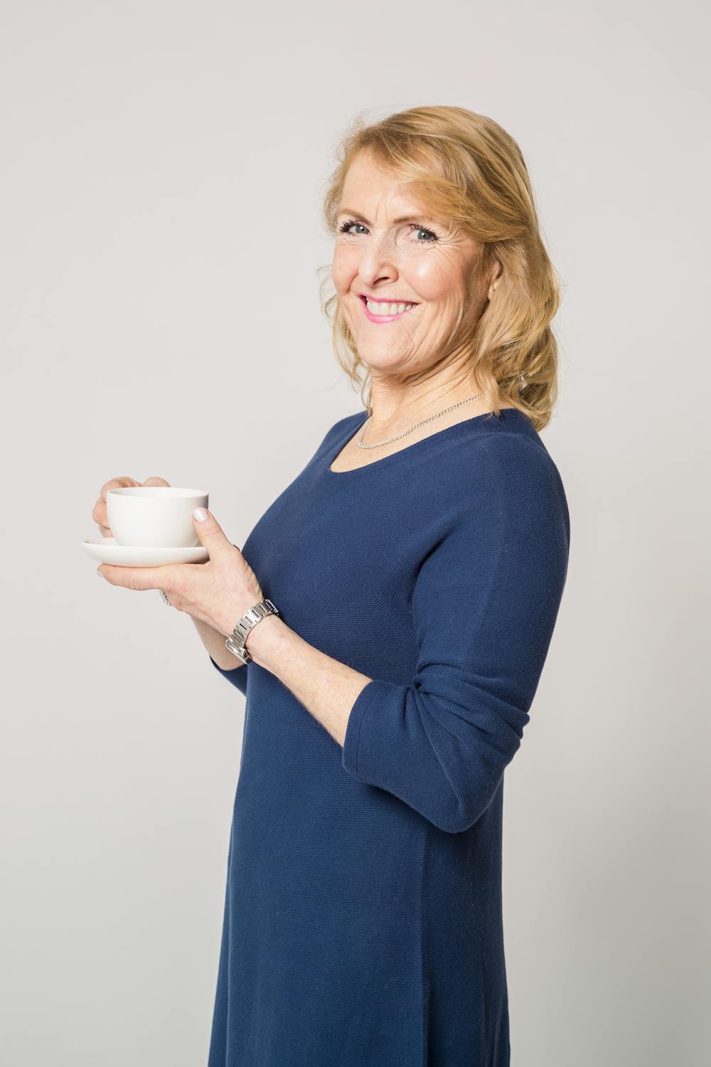 Una mujer sonriente con una taza de té ⏐ Fuente: Pexels