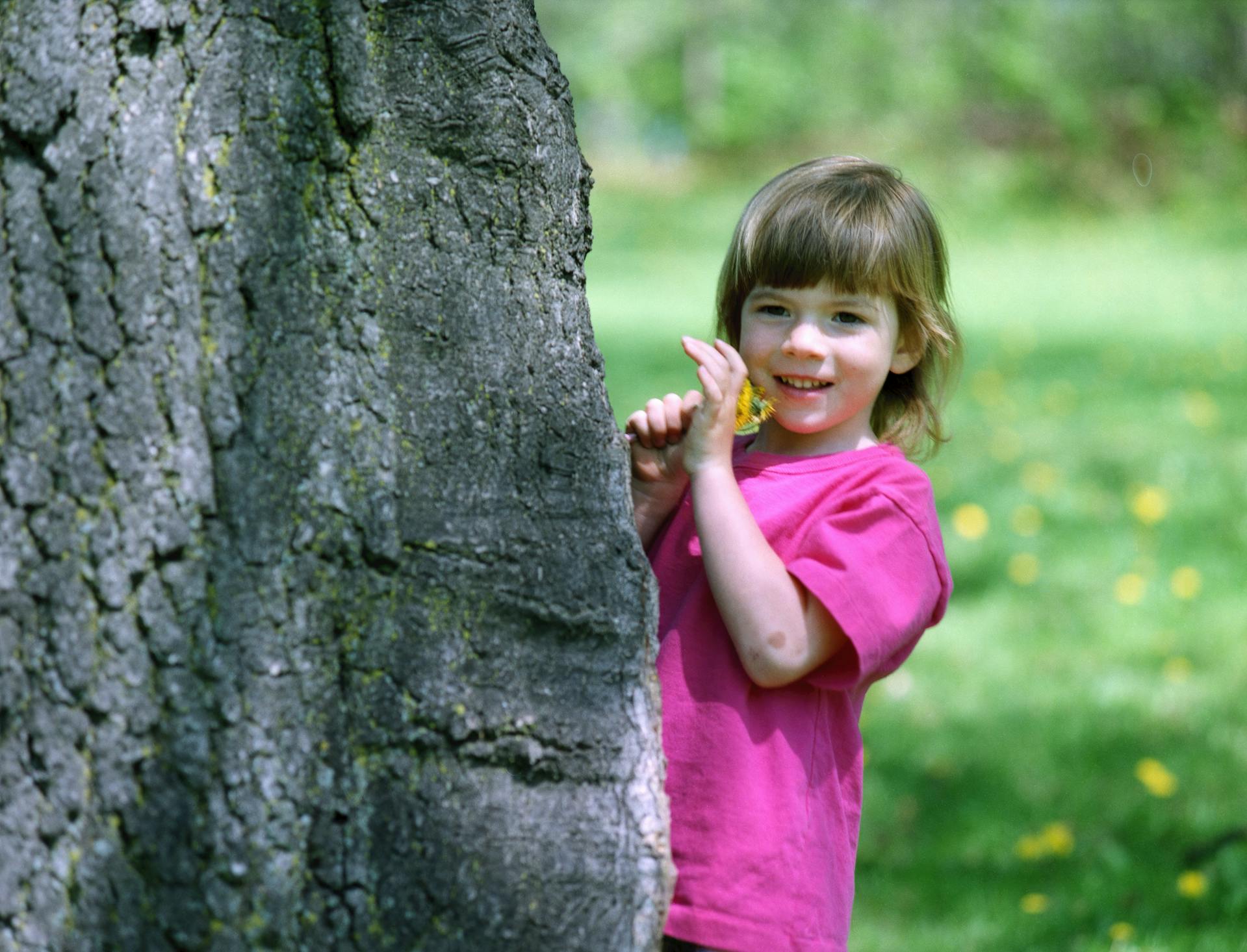 A girl in a pink shirt standing behind a tree | Source: Pexels