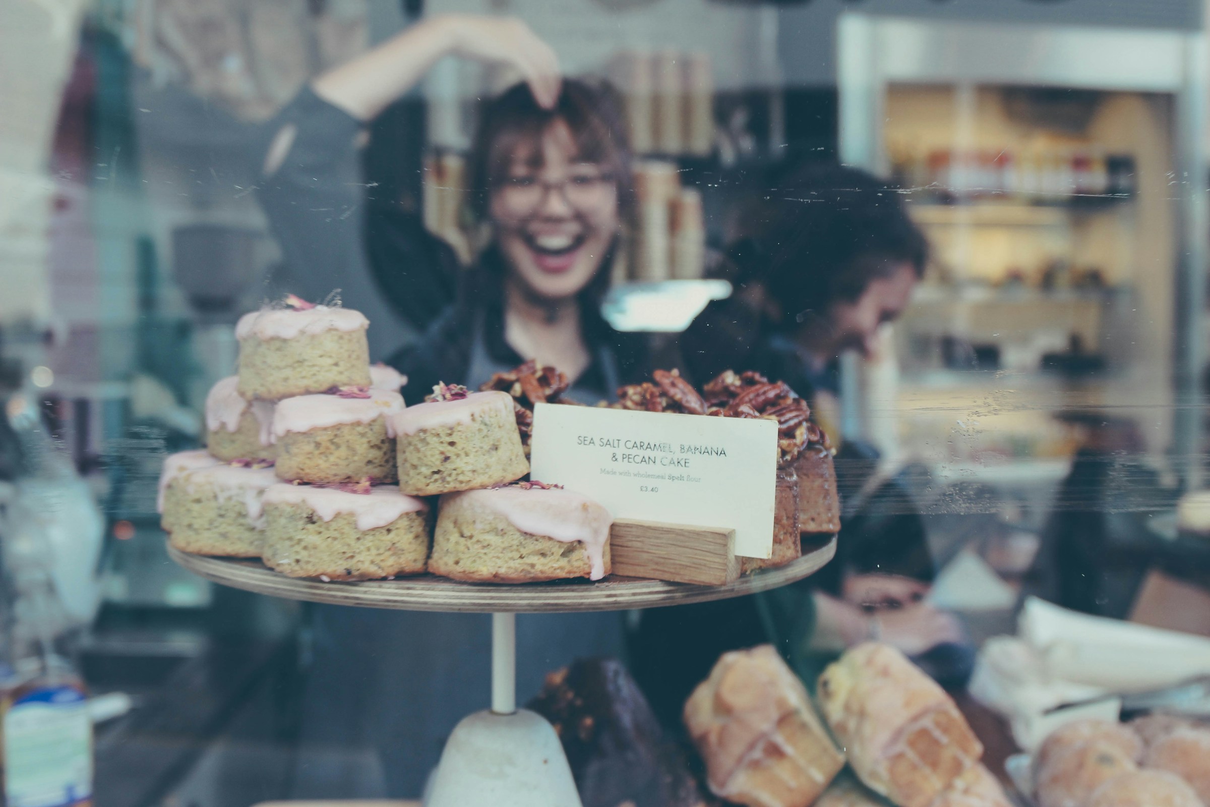 The reflection of a smiling young woman in the glass of a bakery display shelf | Source: Unsplash