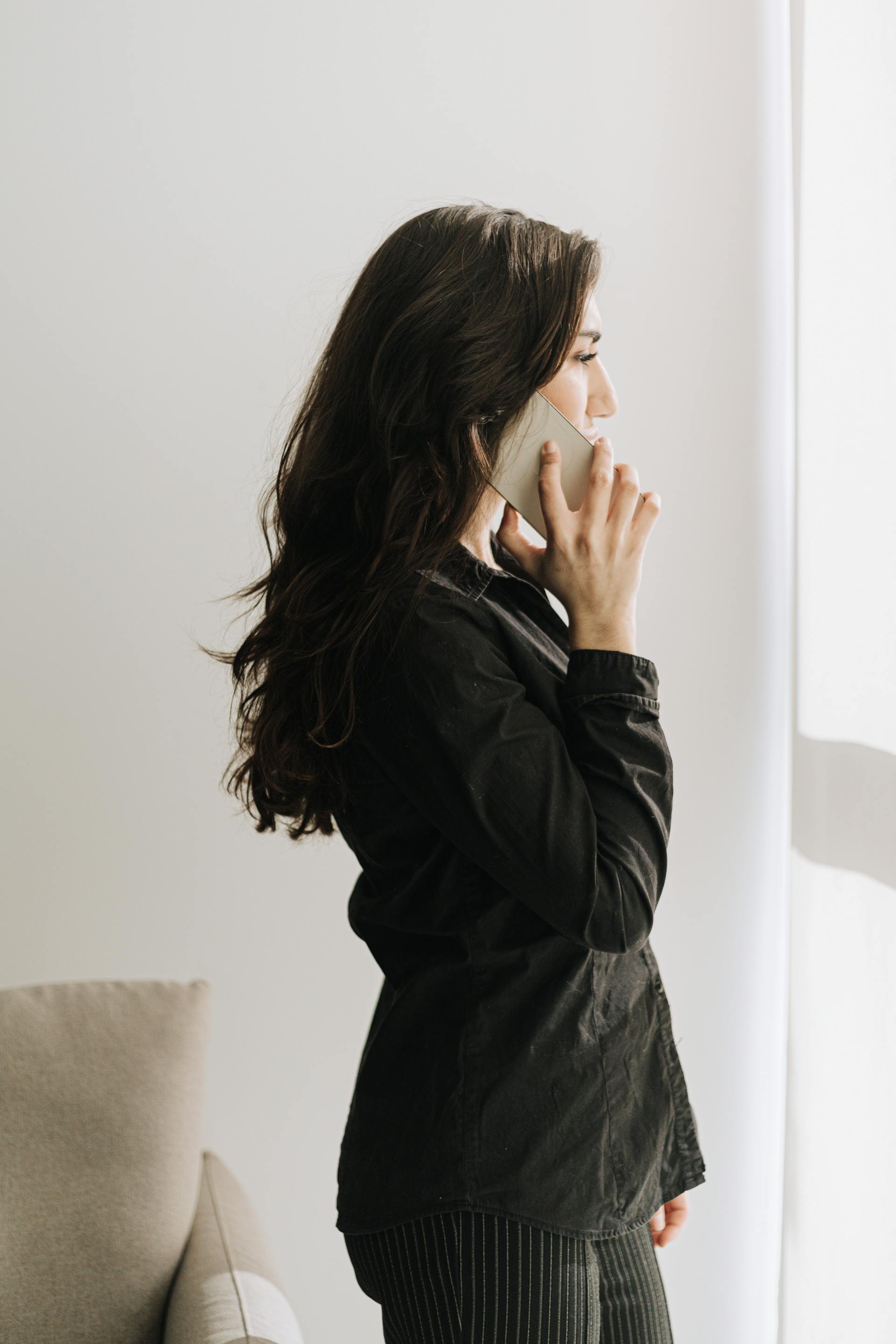 A woman on a phone call standing by a window | Source: Pexels