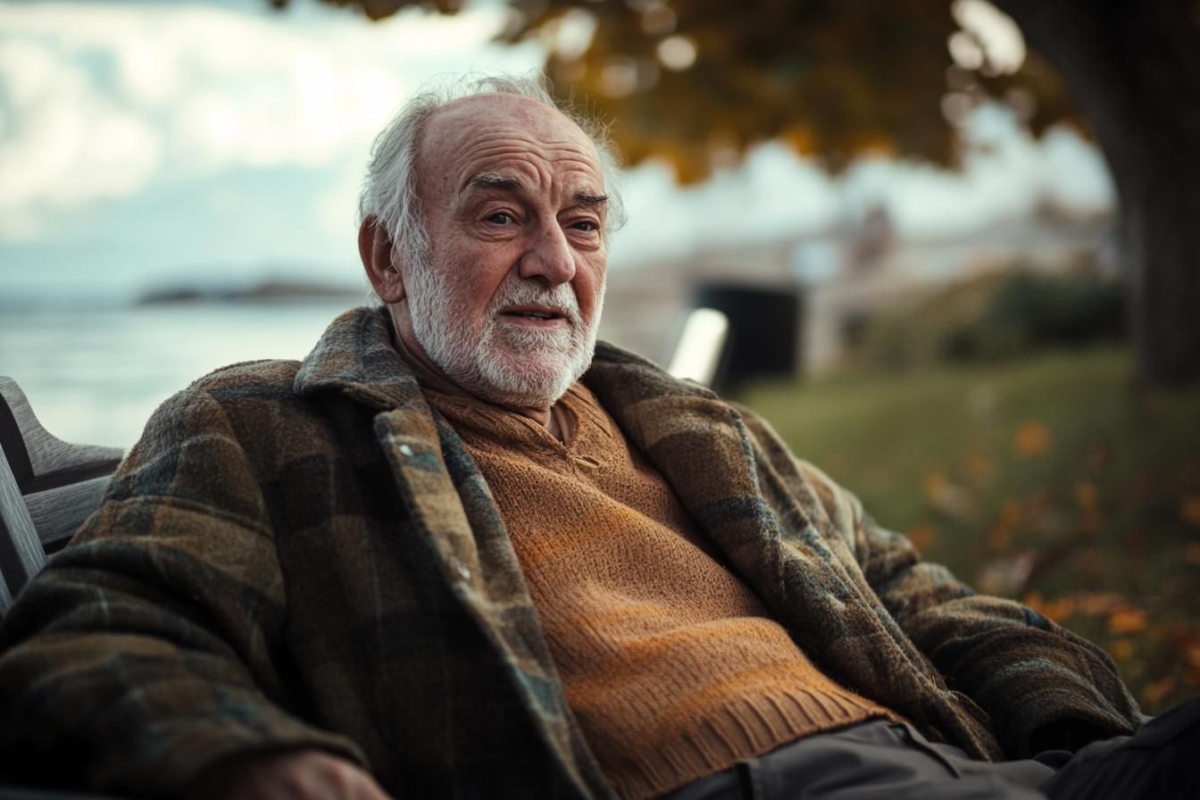 An elderly man sitting on a bench near the ocean | Source: Midjourney