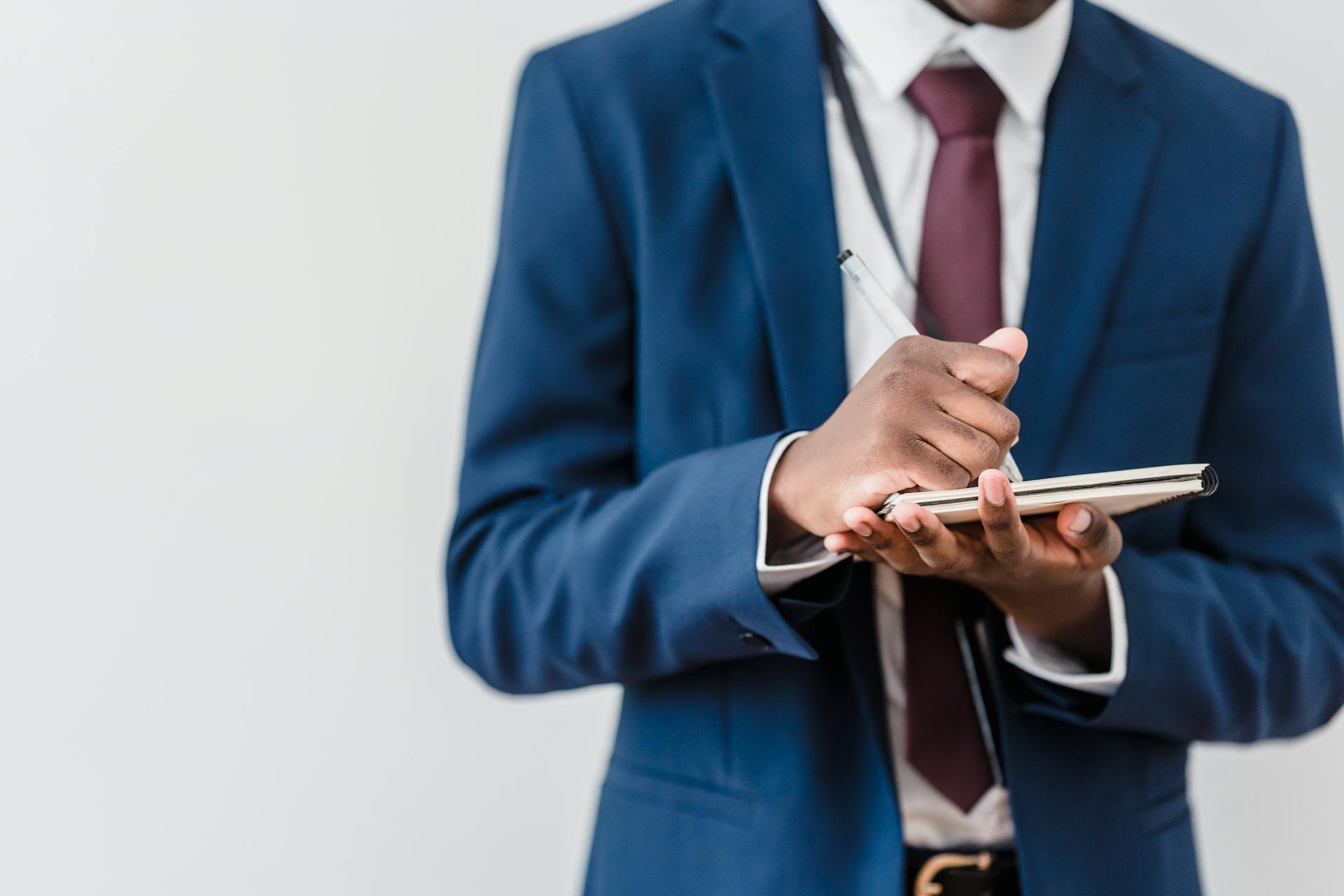 A man in a blue suit writing on a notebook | Source: Pexels