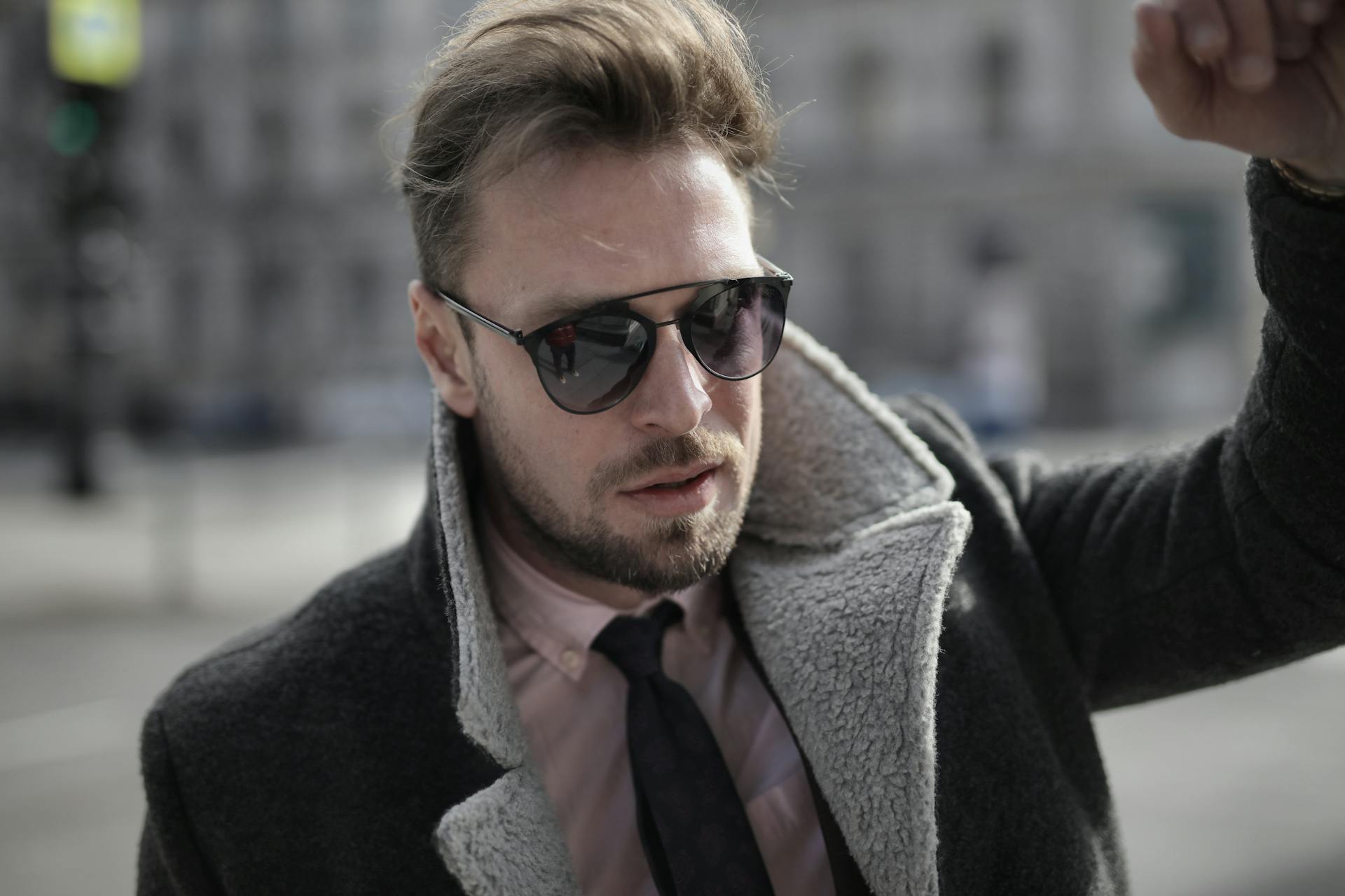 An upset man in a coat and glasses standing with his fist against a wall | Source: Pexels