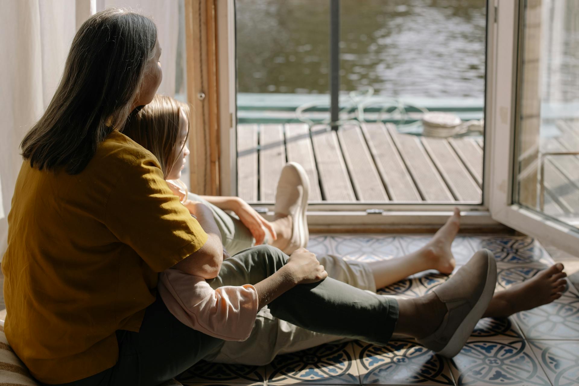 A grandma sitting with her granddaughter on the floor and looking outside | Source: Pexels