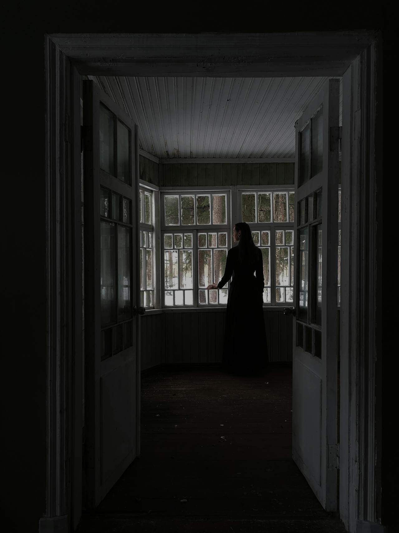 A lonely woman standing near the window of an empty room | Source: Pexels