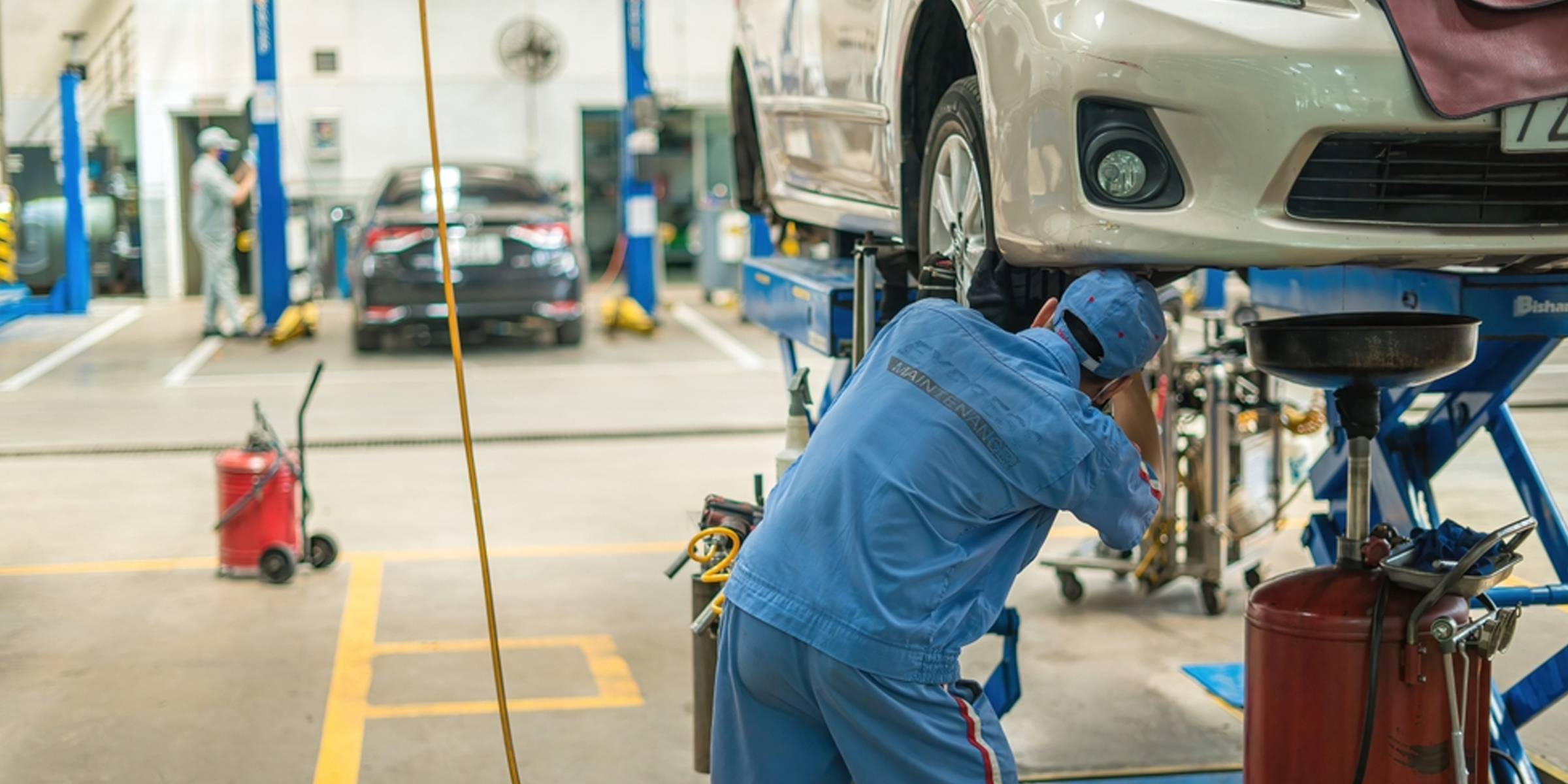 A mechanic works beneath a lifted car at a busy auto repair shop | Source: Shutterstock