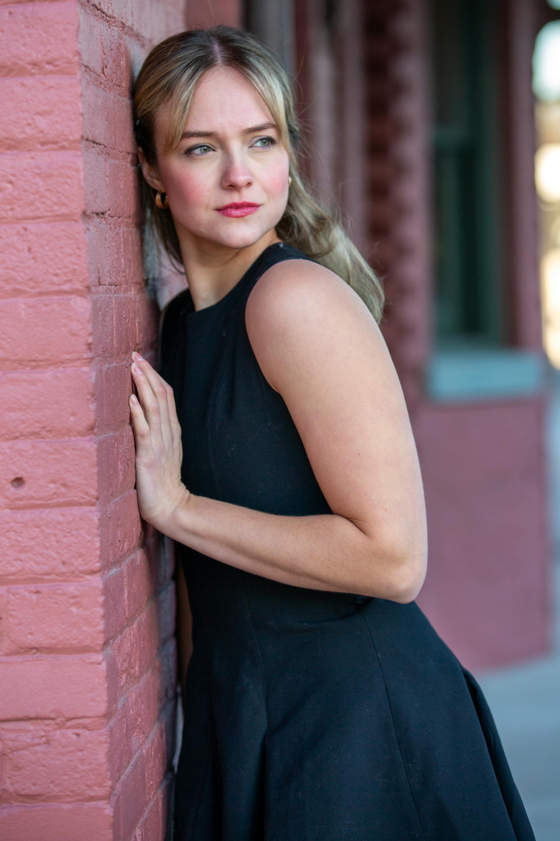 Woman in a black dress leaning against a brick wall | Source: Pexels