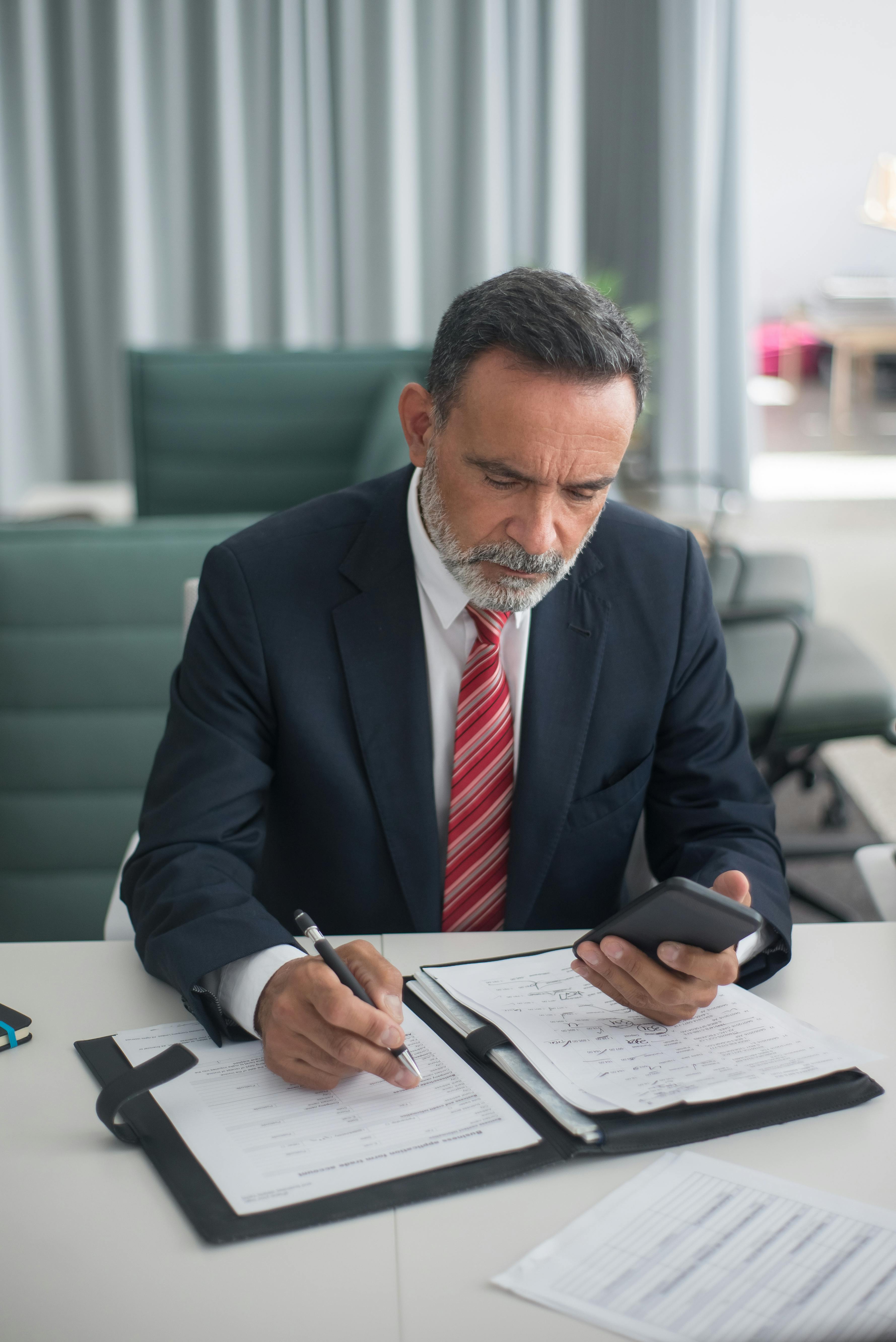 A man holding his phone while writing something | Source: Pexels