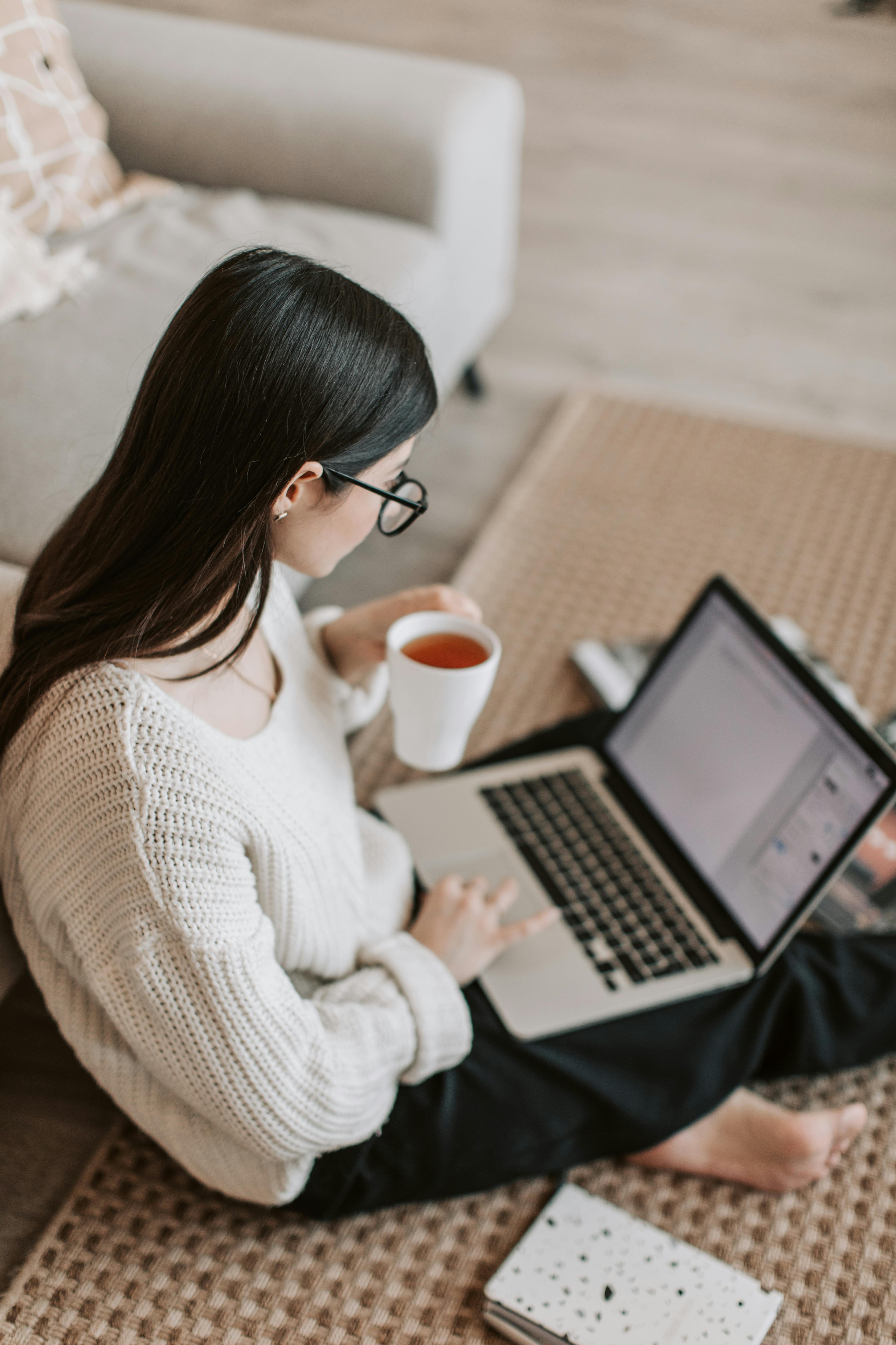 A woman sitting on the floor and using a laptop while holding a cup of beverage | Source: Pexels