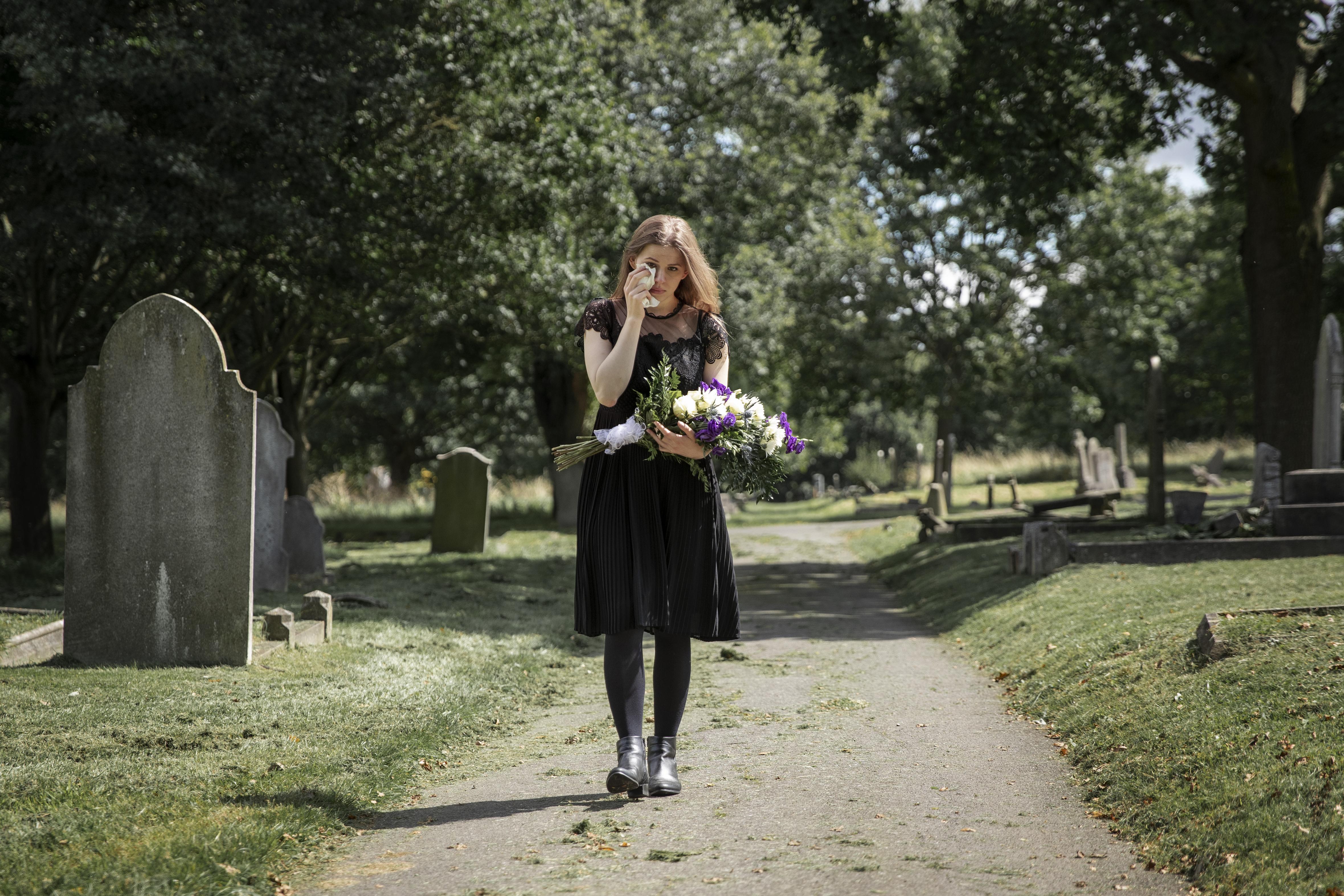 Uma mulher em luto segurando um buquê de flores em um cemitério | Fonte: Freepik