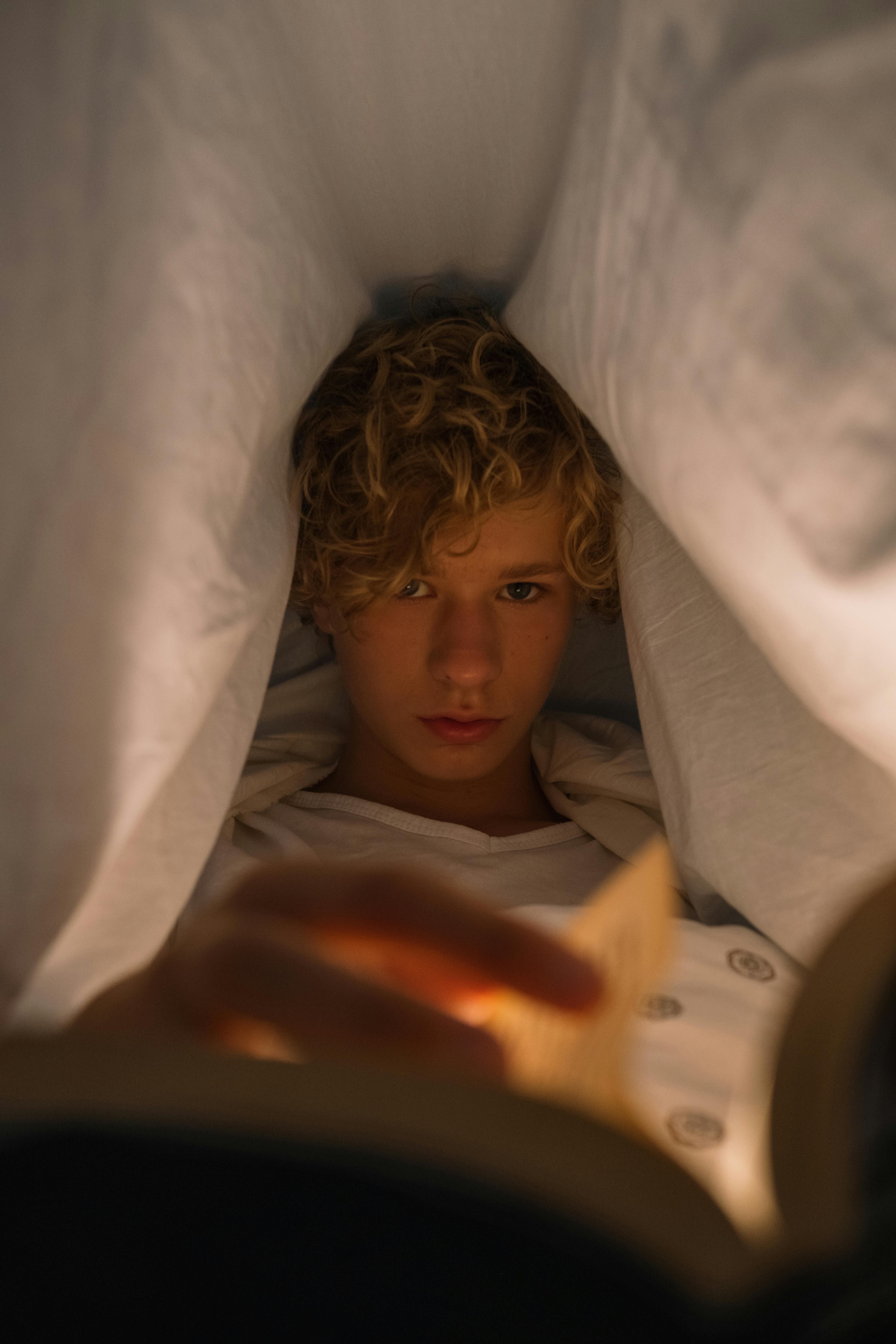 Teenager reading under bedsheet at night | Source: Pexels