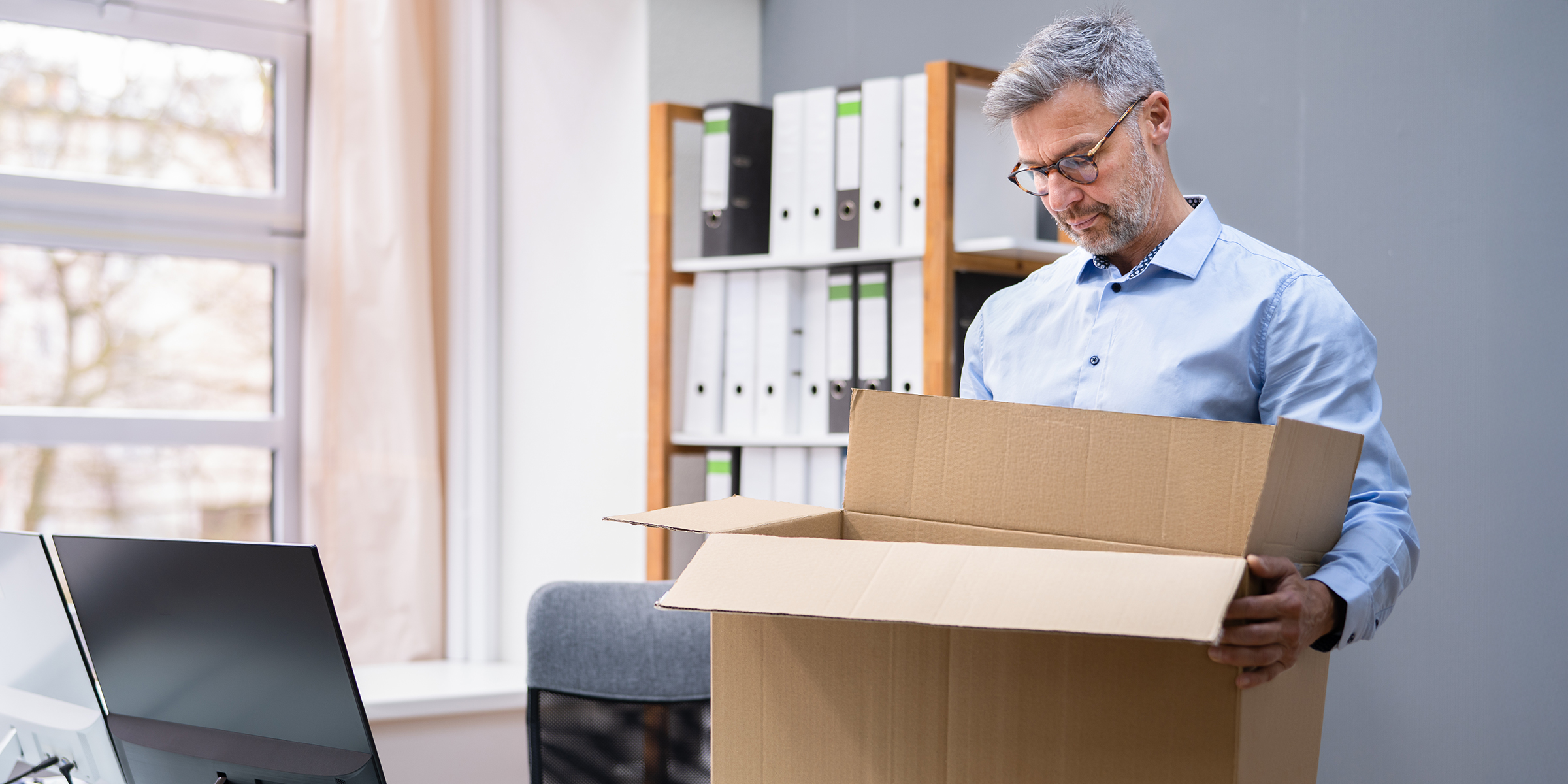 A man standing in his office and looking down at an open cardboard box as he packs up his belongings | Source: Shutterstock