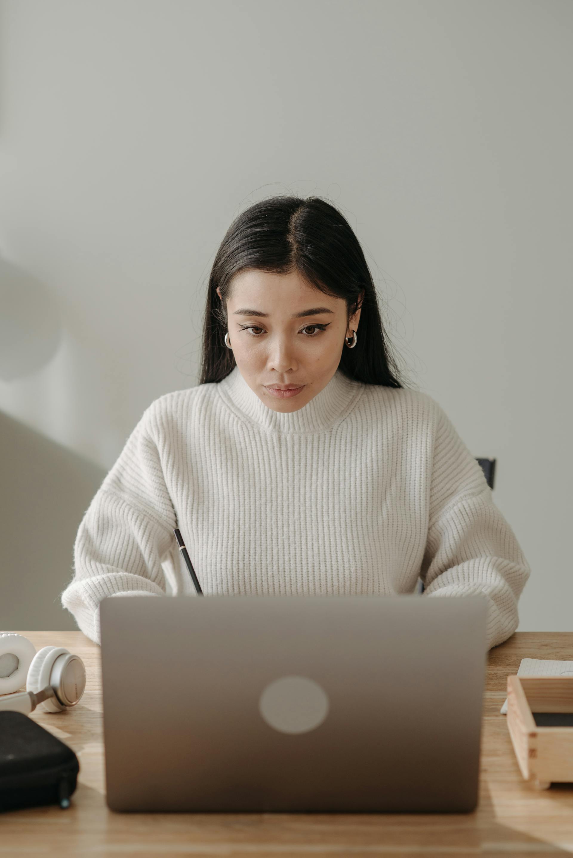 A woman with dark hair wearing a white sweater looking intently at a laptop | Source: Pexels