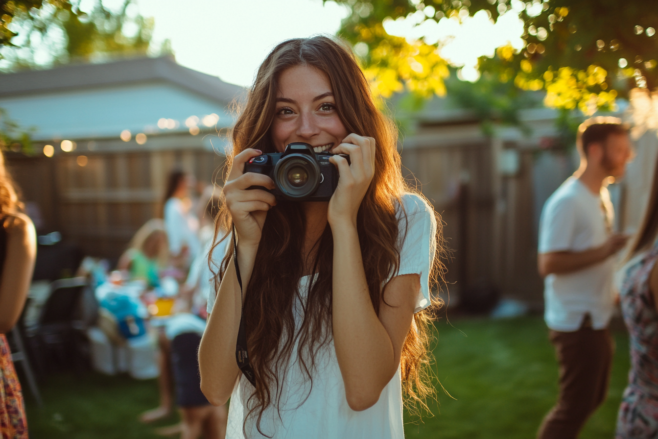 Woman holding a camera and smiling at a backyard birthday party | Source: Midjourney