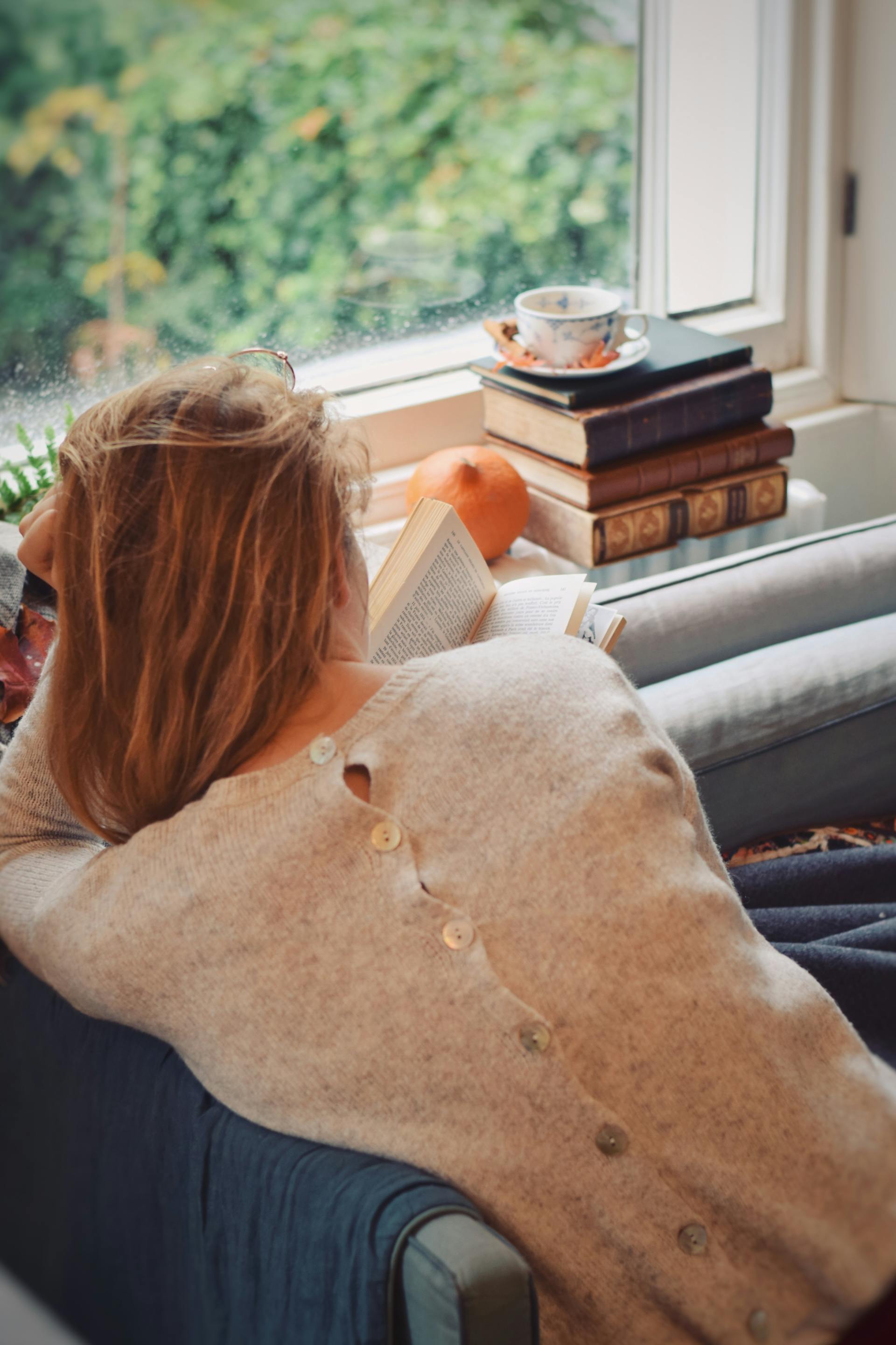 Back view of a woman sitting by the window and reading a book | Source: Pexels