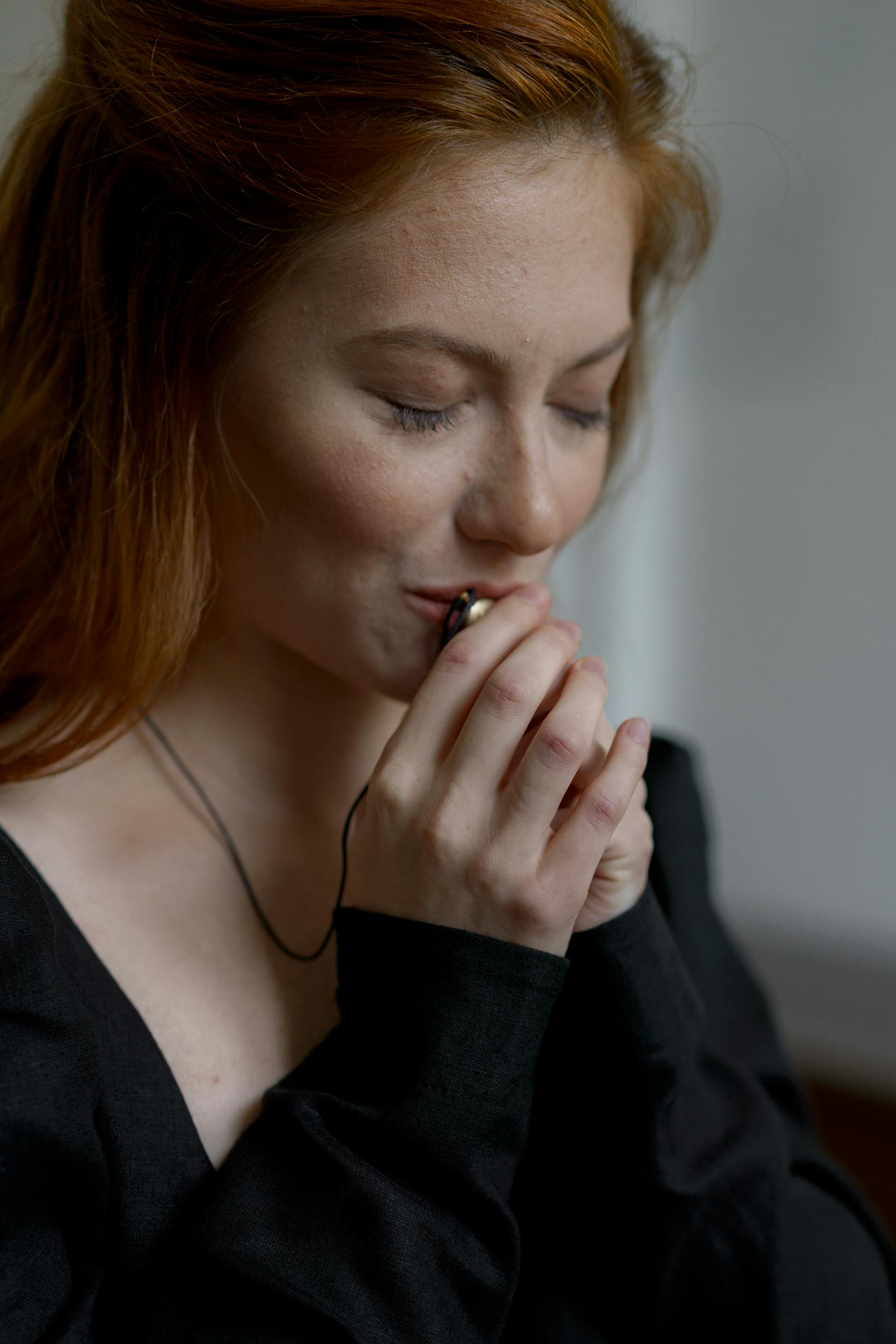 A woman in a black dress kissing her necklace | Source: Pexels
