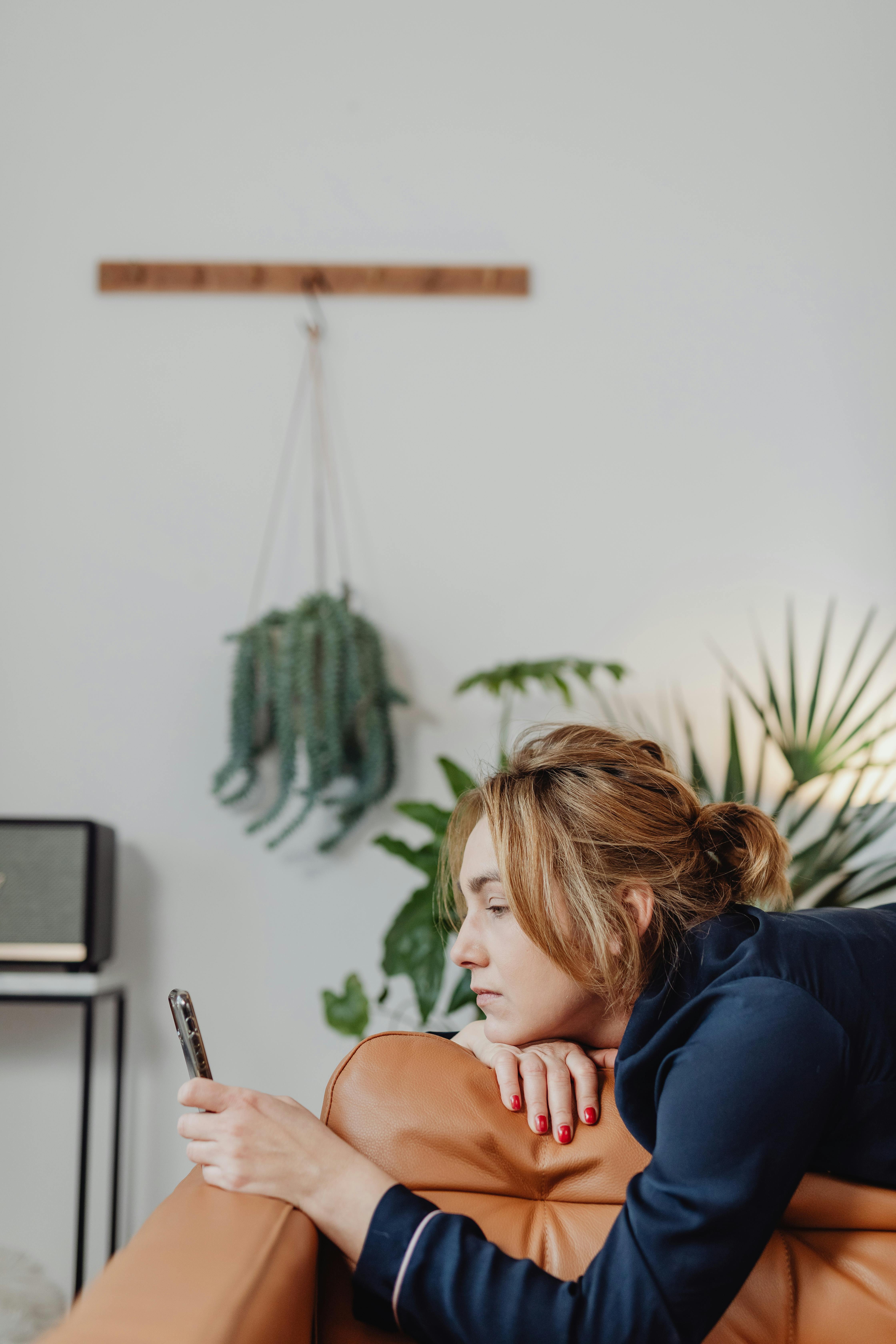 Woman lying down on a brown leather couch looking at her cellphone | Source: Pexels