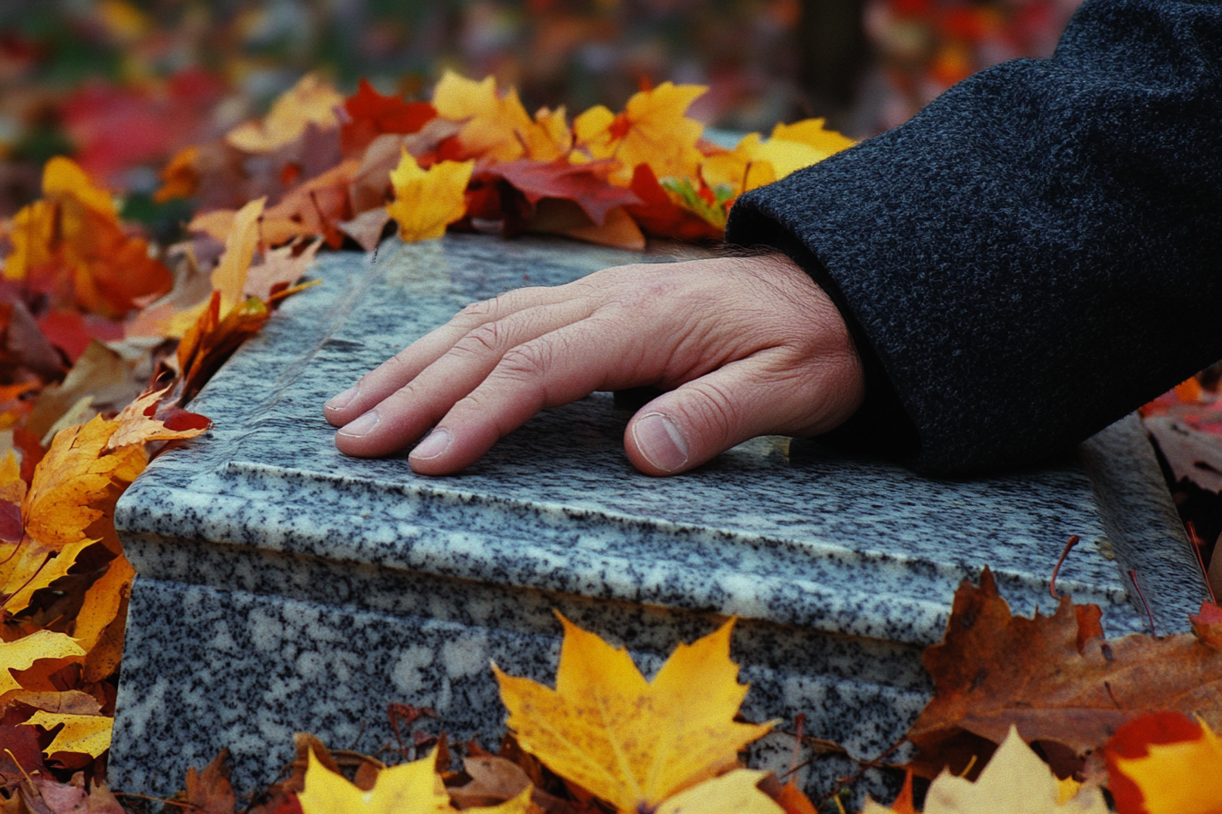 A man's hand resting on a gravestone | Source: Midjourney