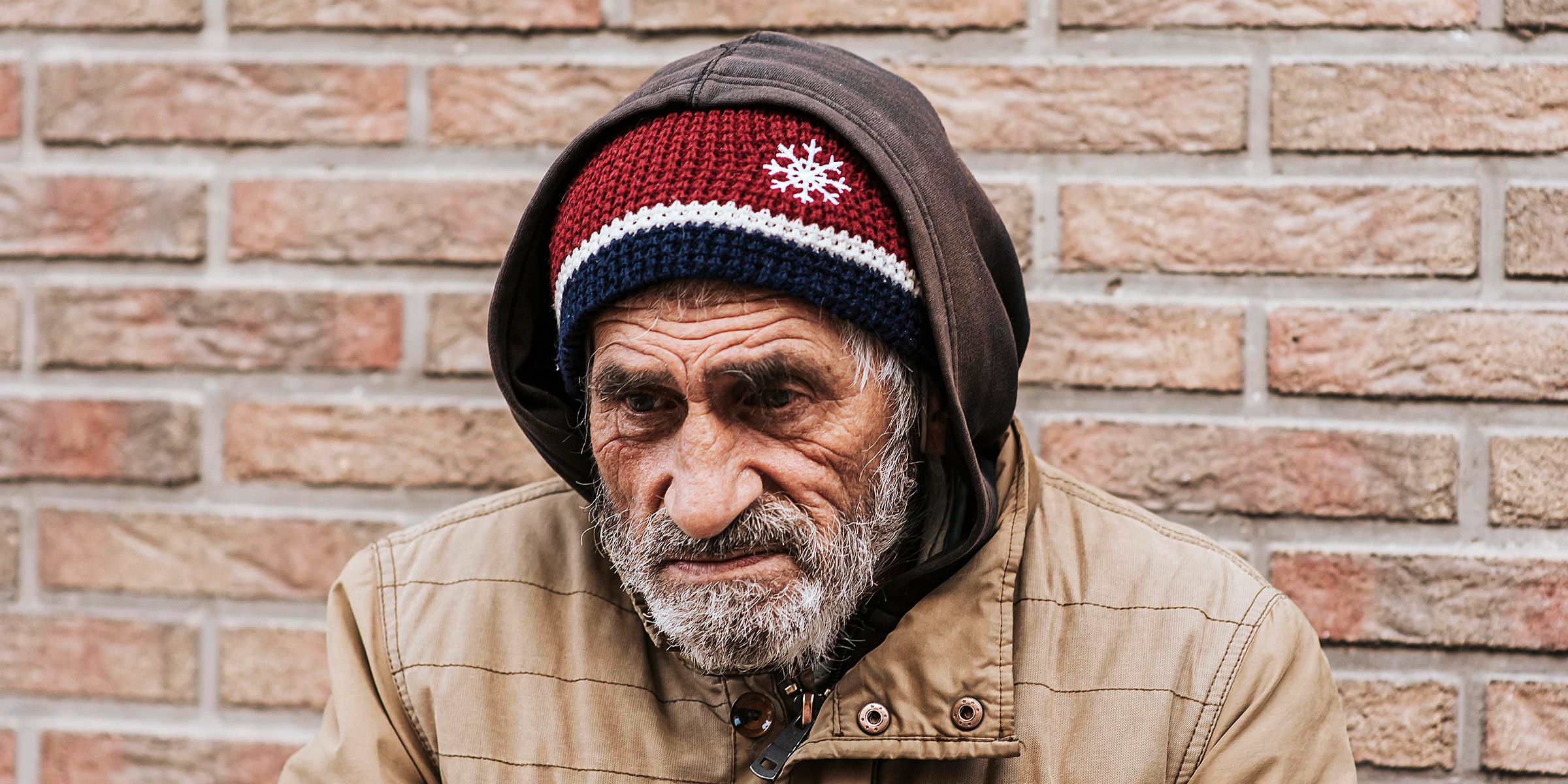 An elderly man standing beside a brick wall | Source: Freepik