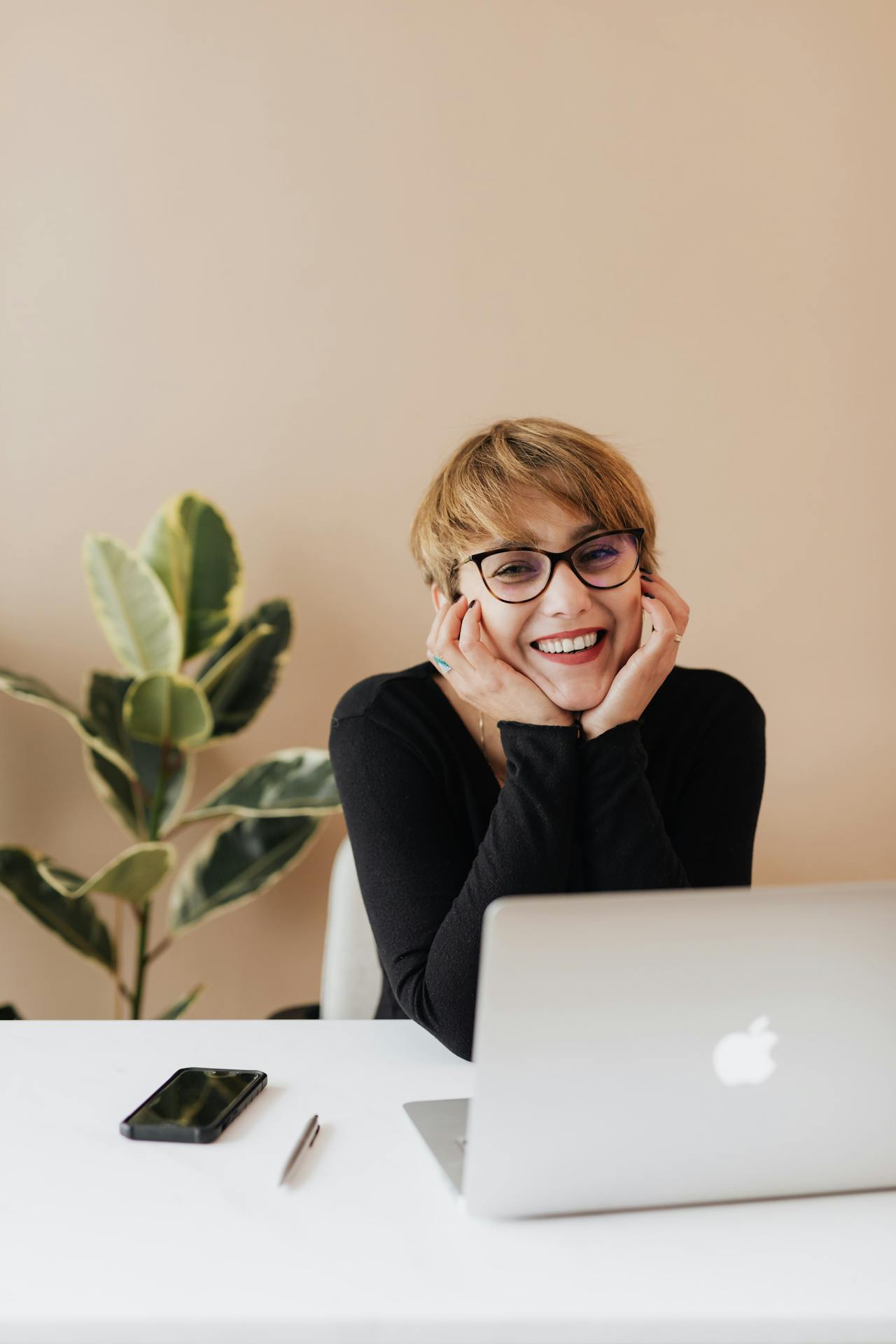A woman smiling while seated at a table with her laptop | Source: Pexels