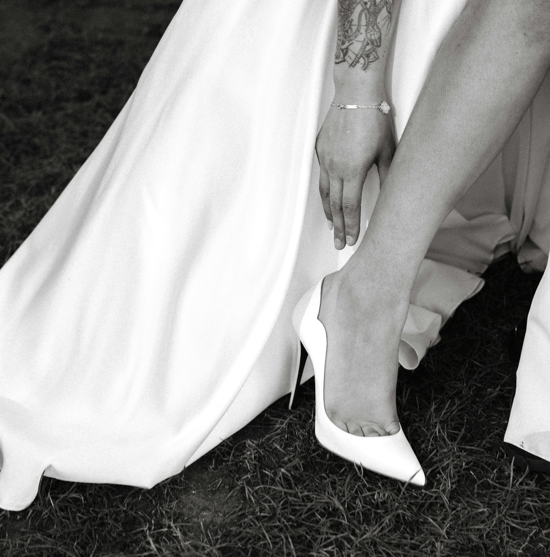A close-up shot of a bride reaching for her heels while standing on the grass | Source: Pexels
