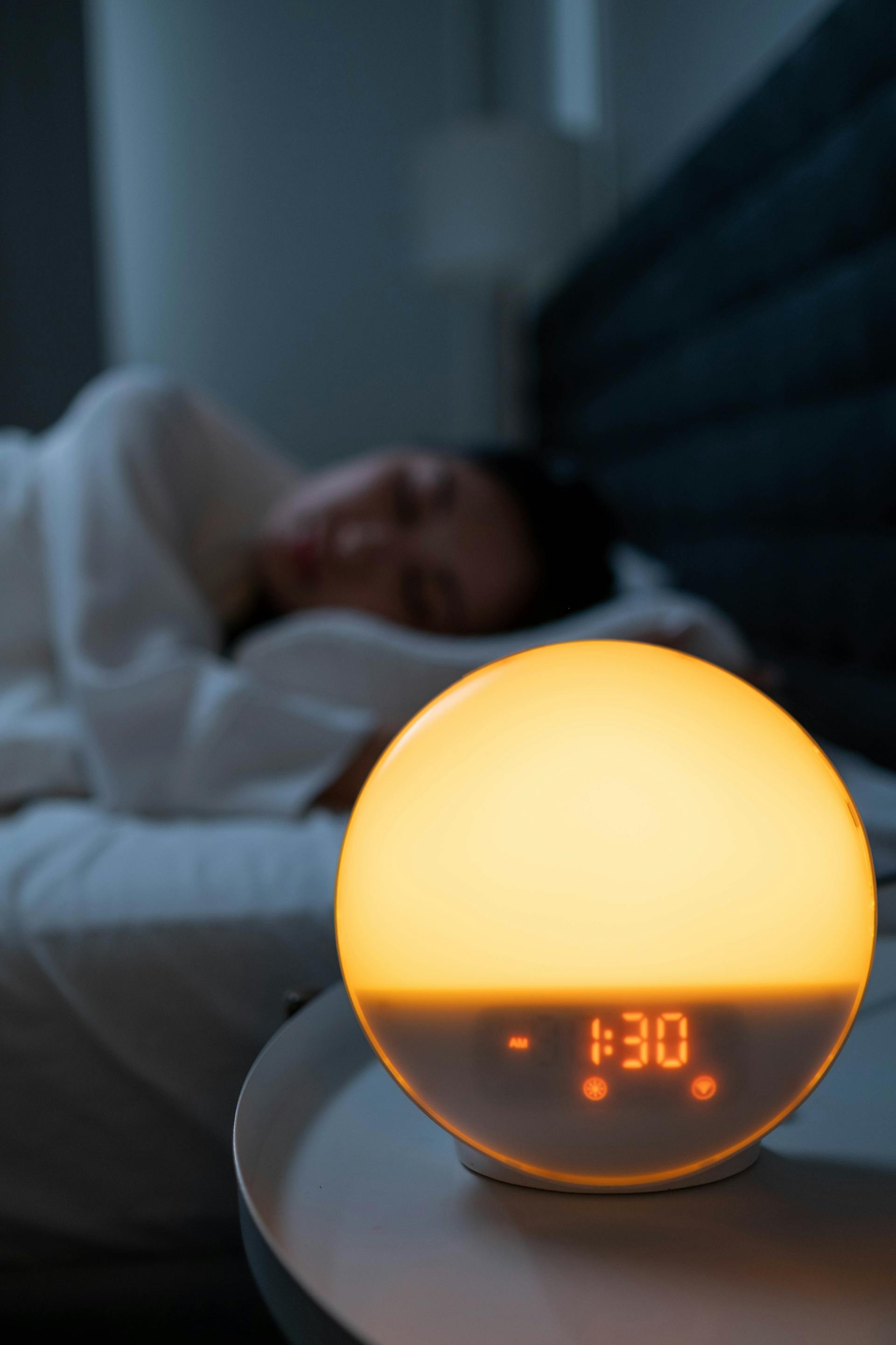 A clock on a night stand with a woman sleeping in the background | Source: Pexels