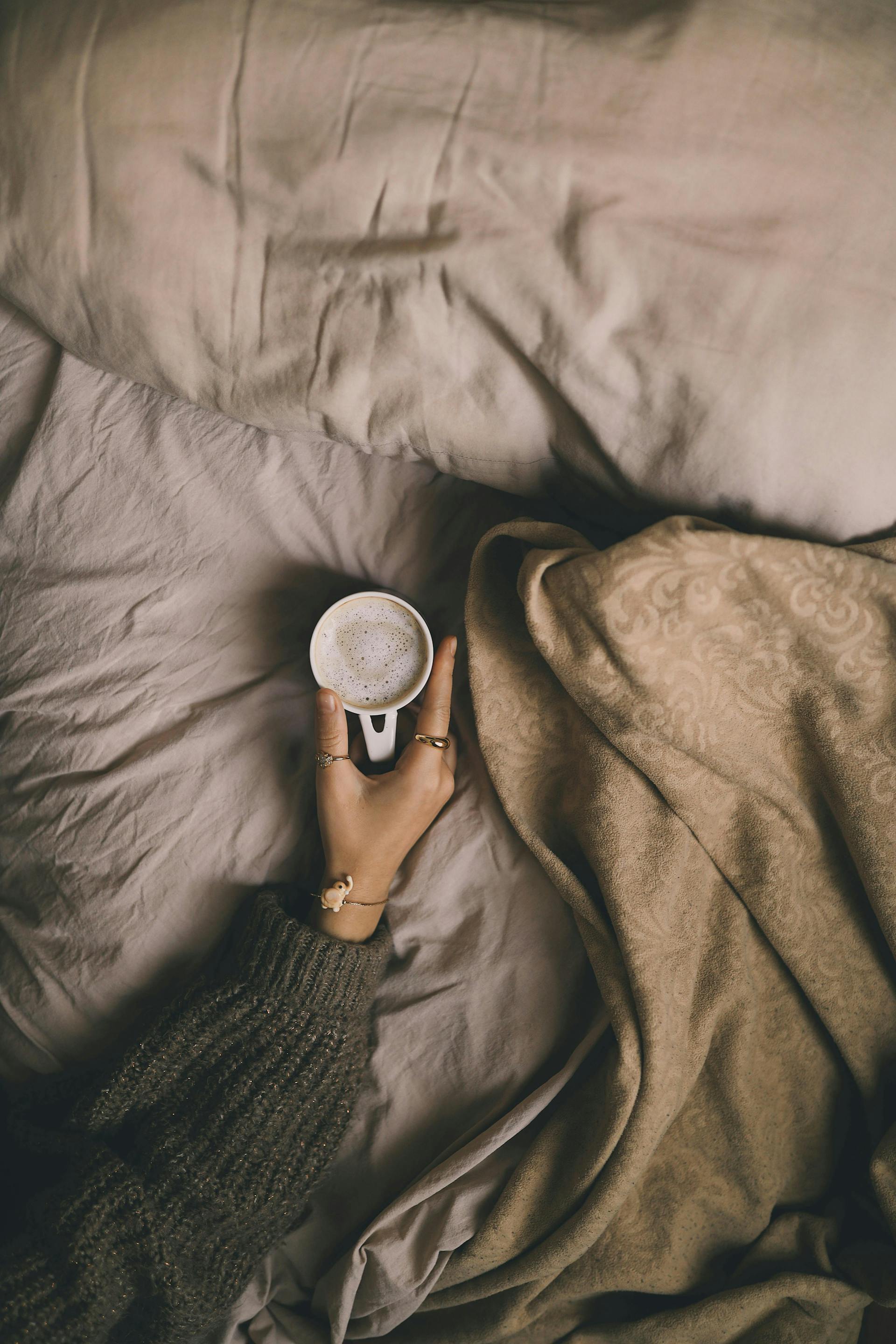 A close-up shot of a woman holding a cup of coffee in bed | Source: Pexels