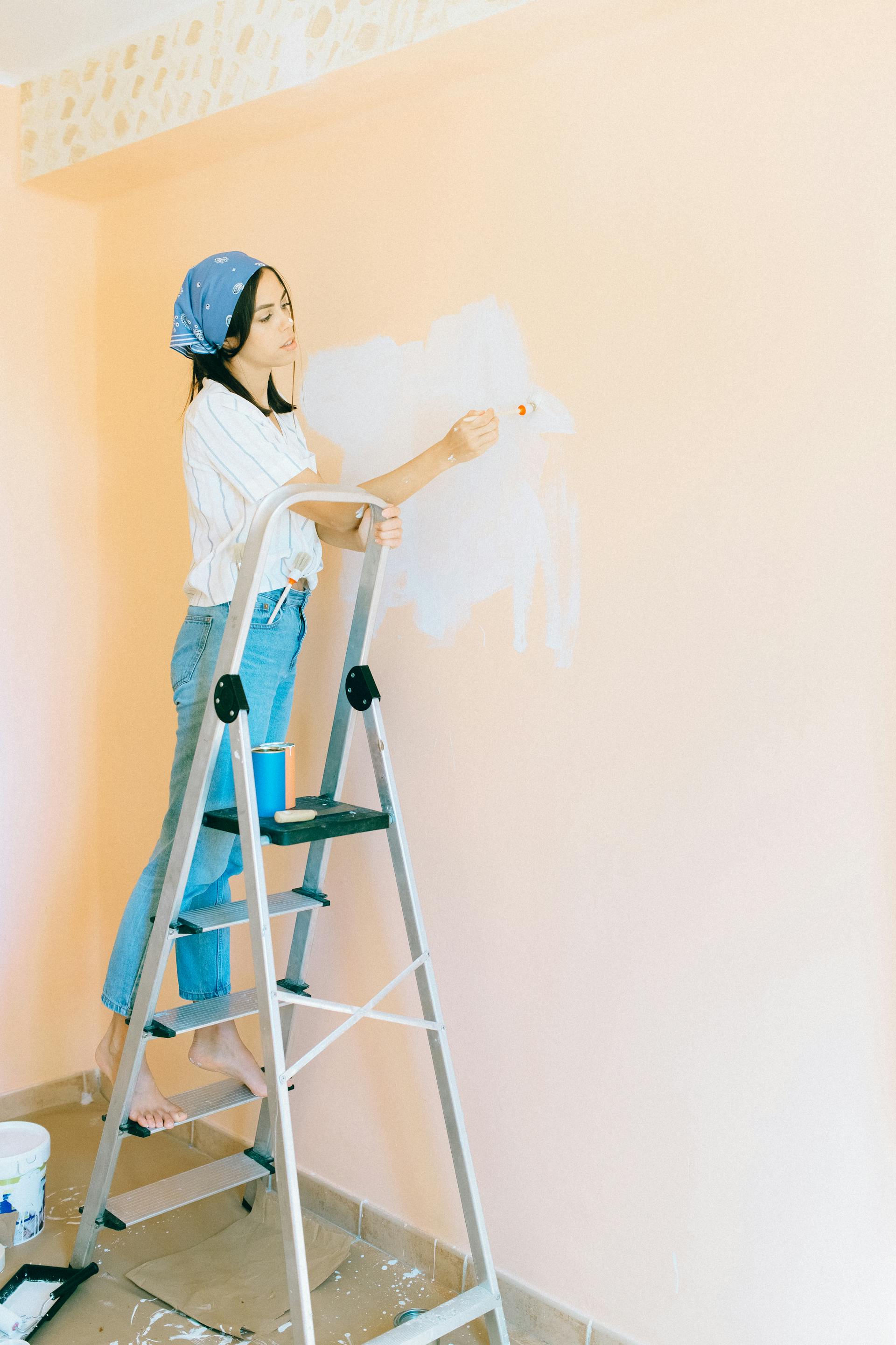 A woman standing on a stepladder and painting a wall | Source: Pexels