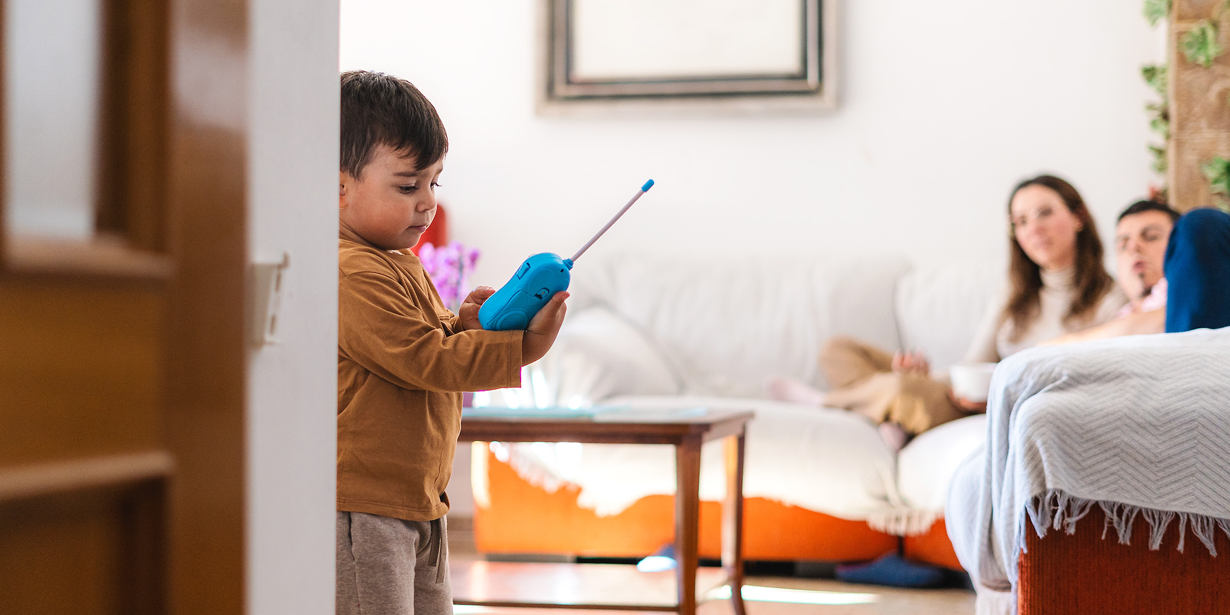 A little boy playing with a blue walkie-talkie while two adults watch from the couch | Source: Shutterstock