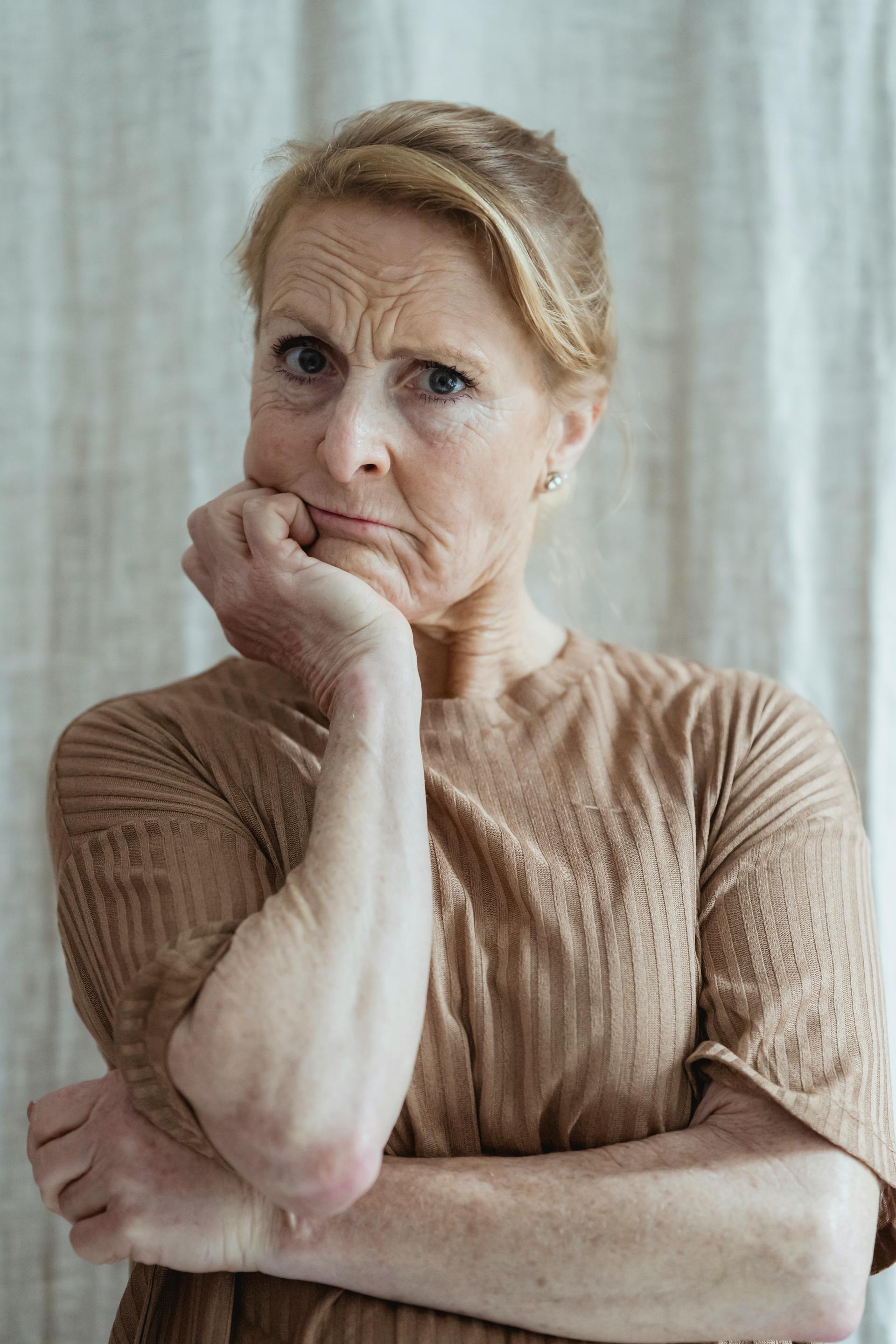 A worried mature woman in a brown sweater with her hand on her chin looking forward | Source: Pexels