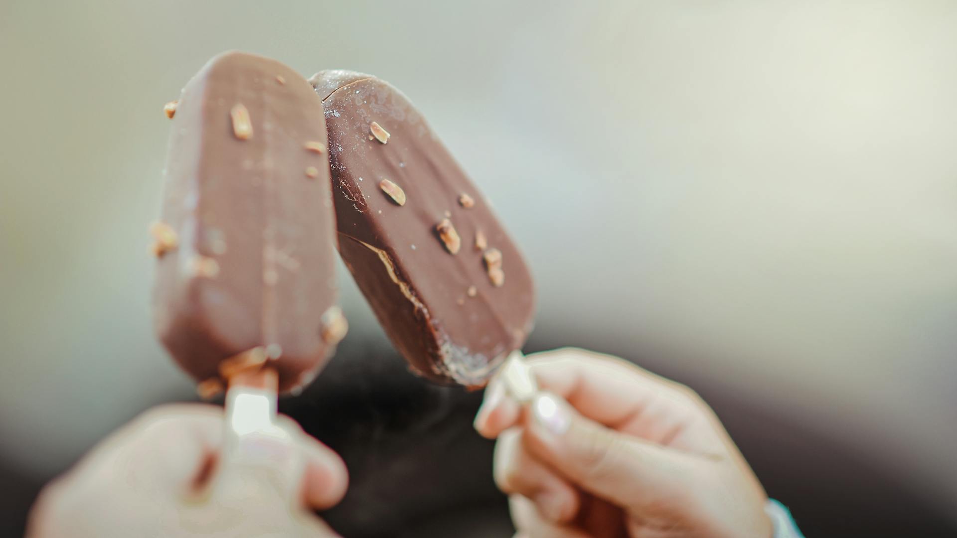 A close-up of two hands holding chocolate ice cream sticks | Source: Pexels