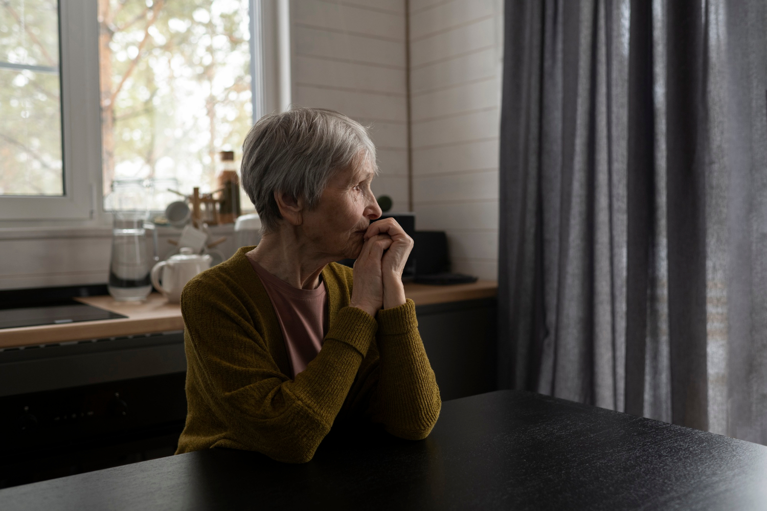 A thoughtful senior woman seated at a table | Source: Freepik