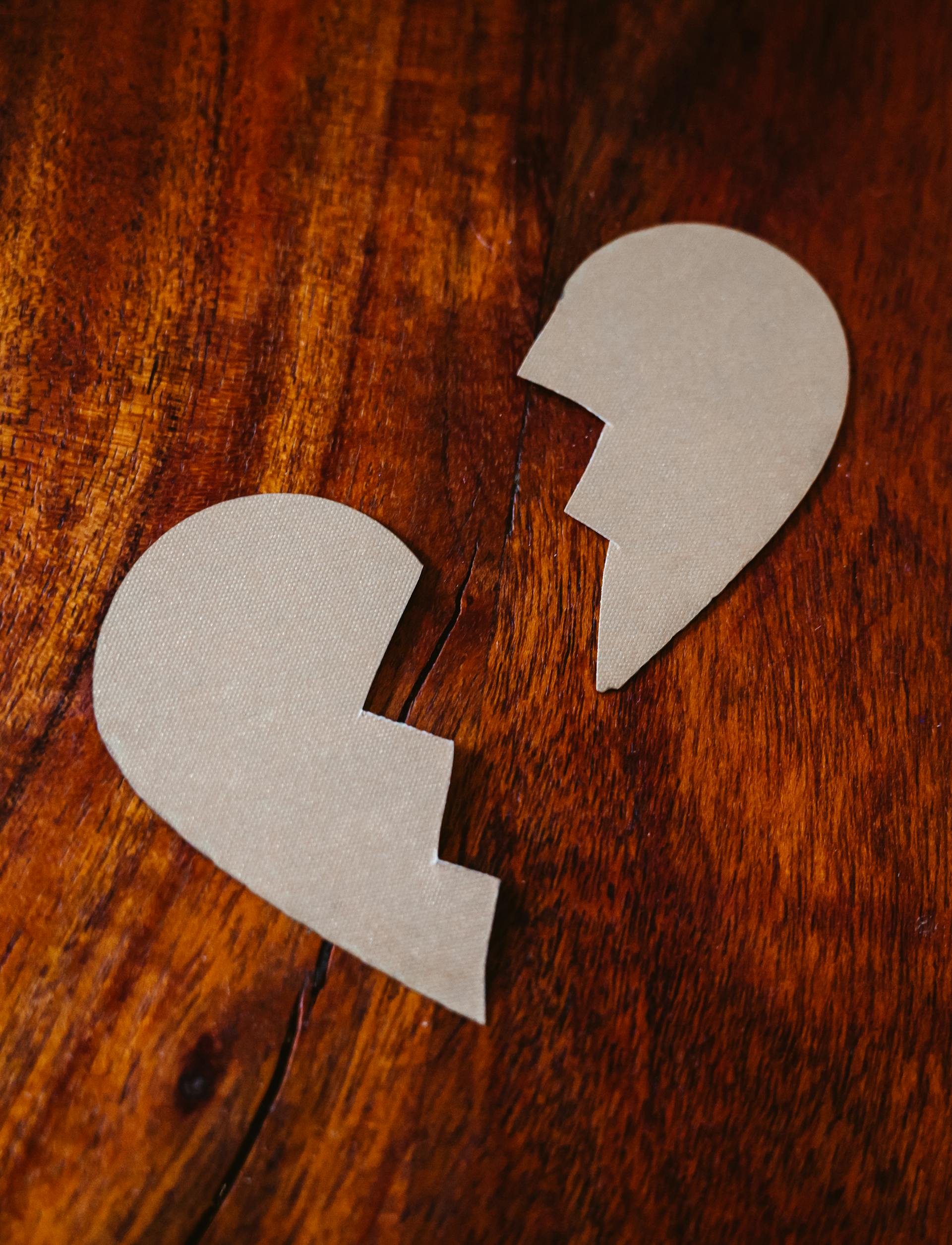 Cardboard pieces in the shape of a broken heart on a wooden surface | Source: Pexels