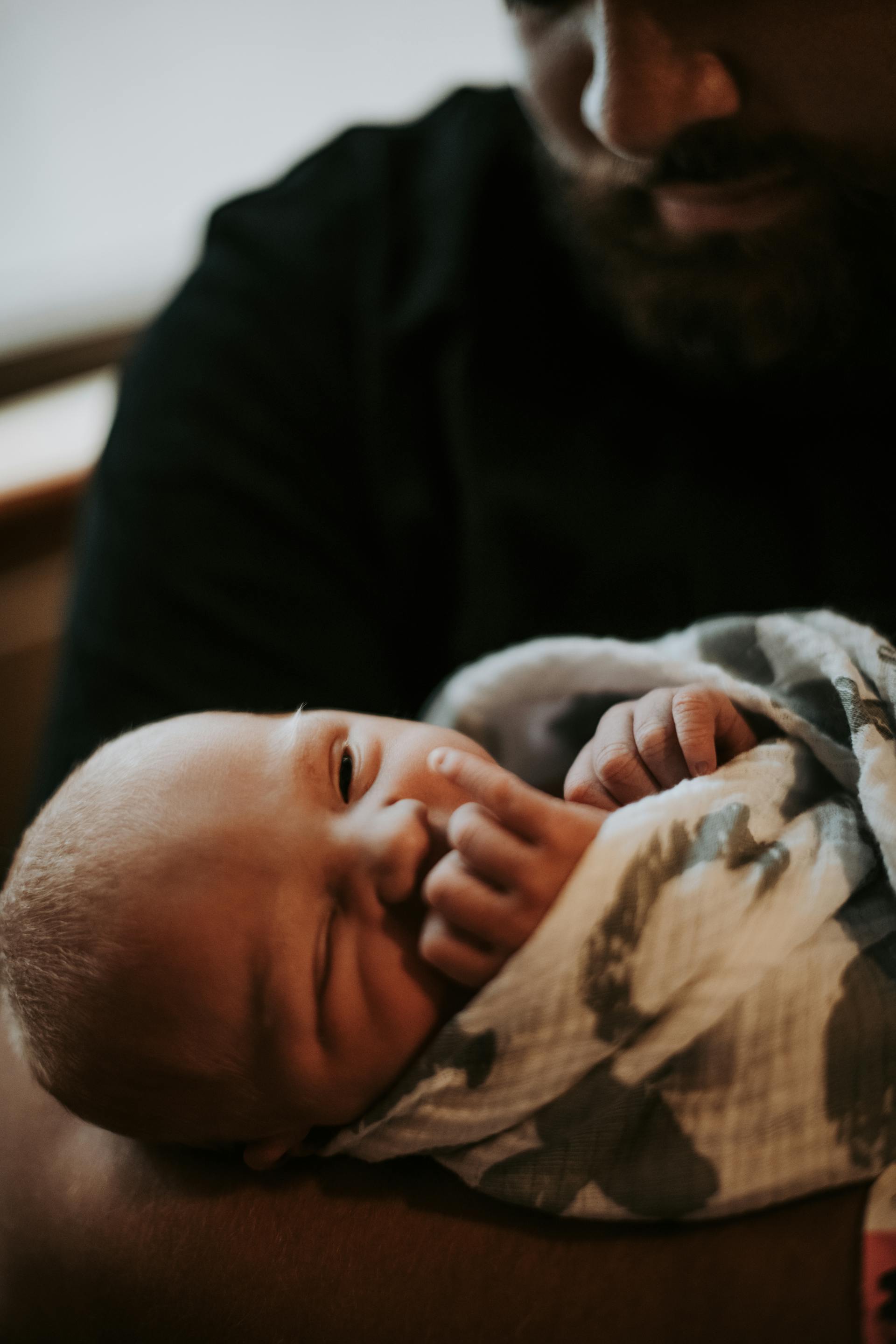 A baby swaddled in a blanket being held by a man | Source: Pexels