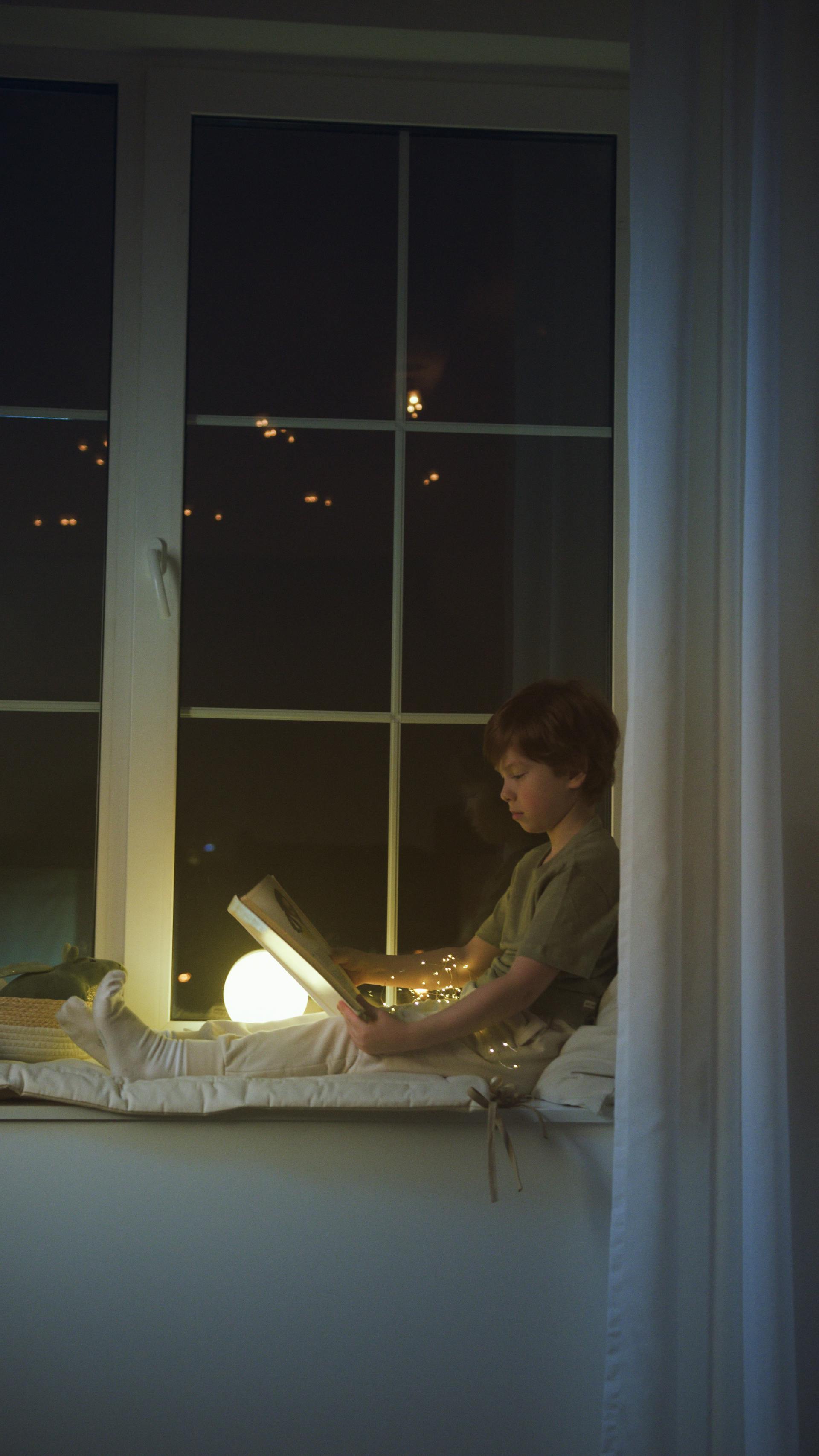 A little boy reading a book while sitting on a window sill | Source: Pexels