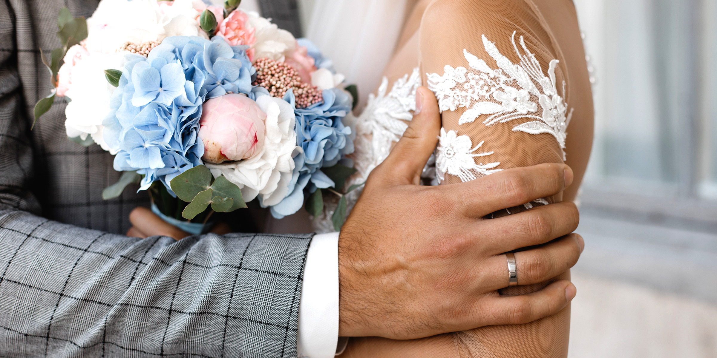 A groom gently holds his bride, their hands wrapped around a bouquet of pastel flowers | Source: Freepik